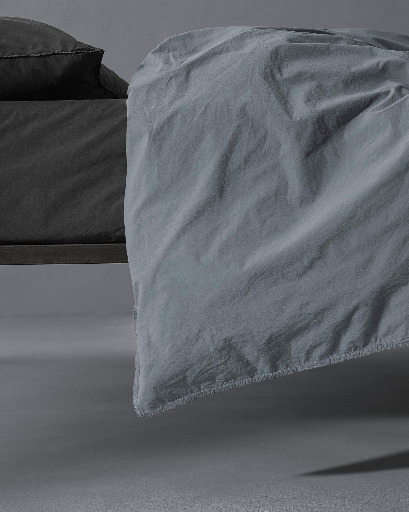 Society Limonta Nite duvet cover hem detail in slate blue, draped over bed edge.
