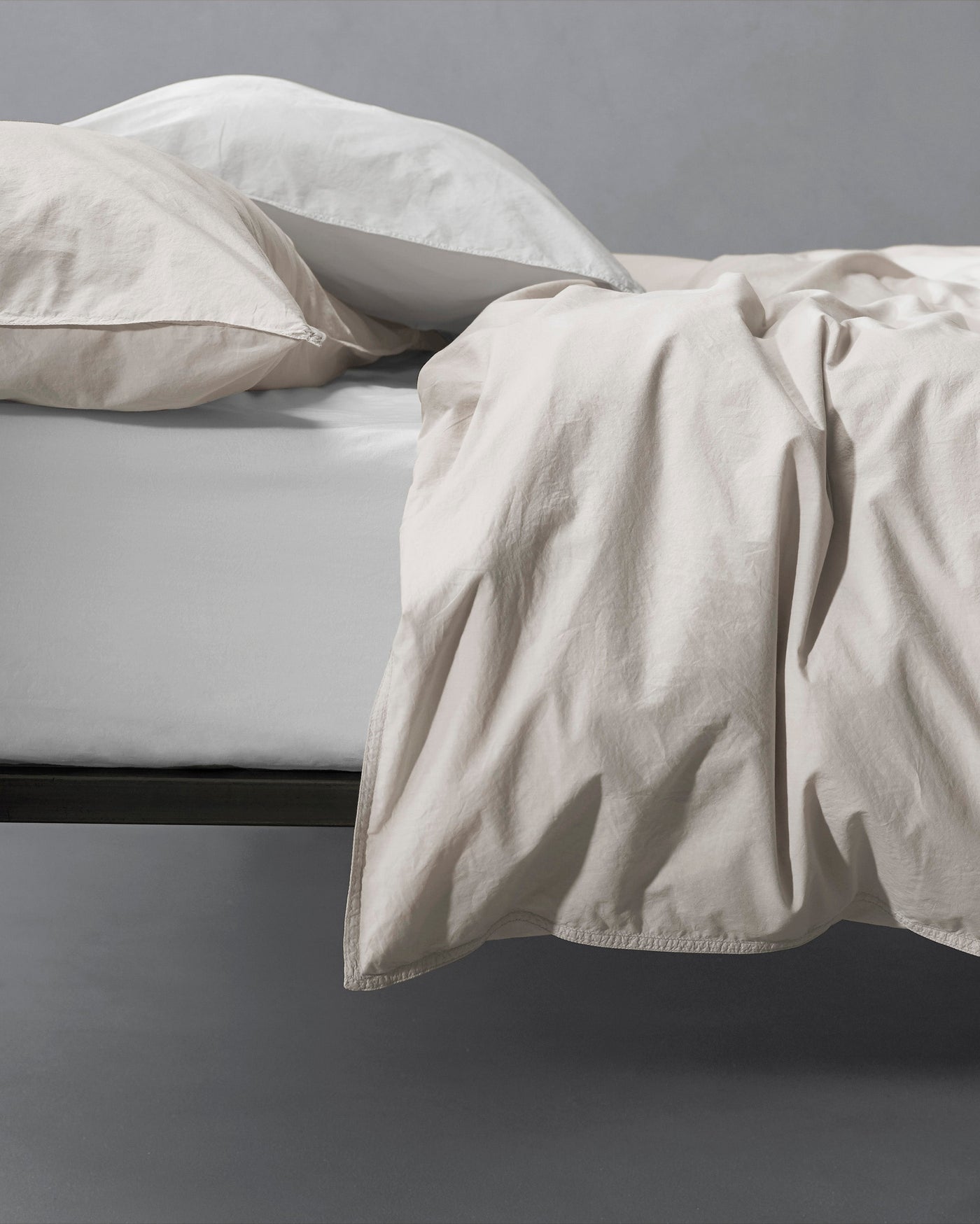 Relaxed sand cotton duvet cover draped over bed edge, softly rumpled texture.
