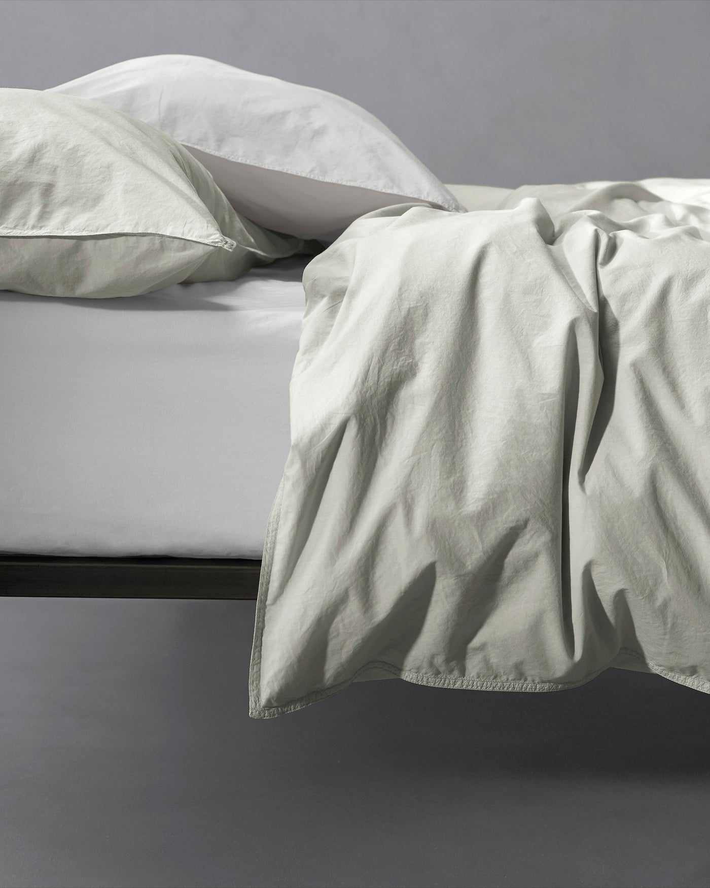 Sage green washed cotton duvet cover draped over bed edge, showing relaxed texture.