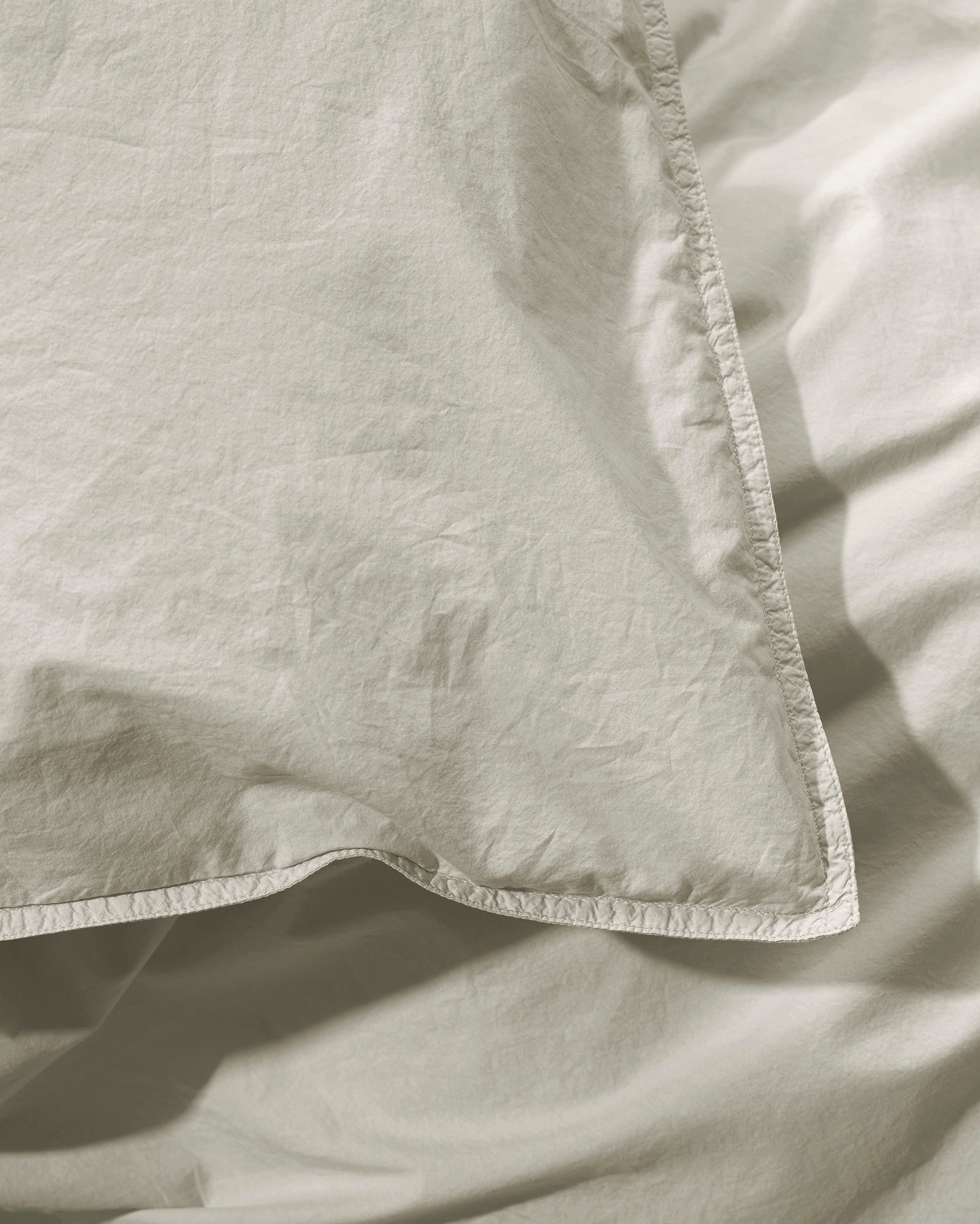 Close-up of Society Limonta Nite duvet cover corner with contrast stitching in sage linen.