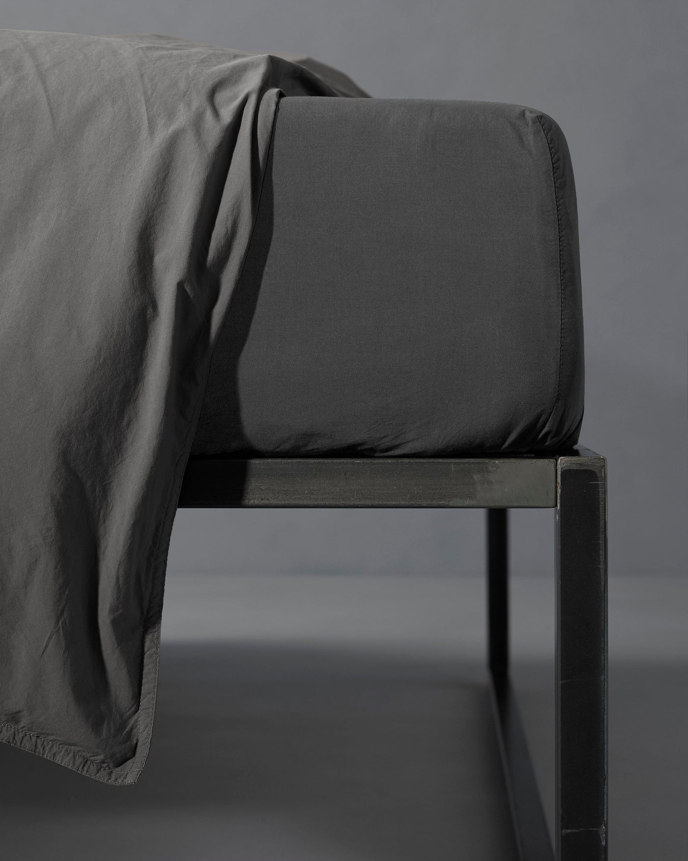 Close-up of Society Limonta Nite fitted sheet corner in charcoal on a dark metal bed frame.