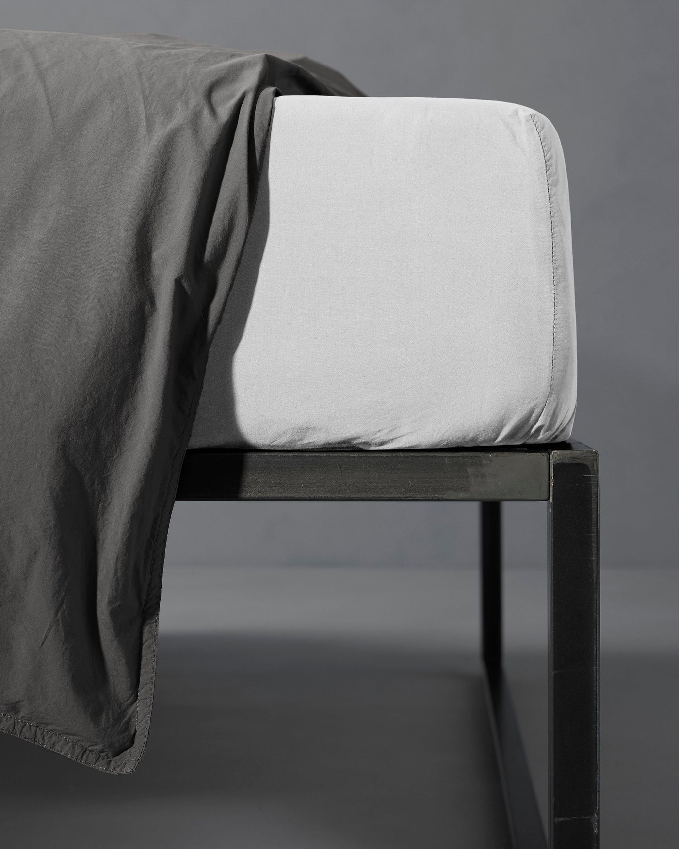 Corner detail of a Society Limonta Nite fitted sheet in ivory on a dark metal bed frame.