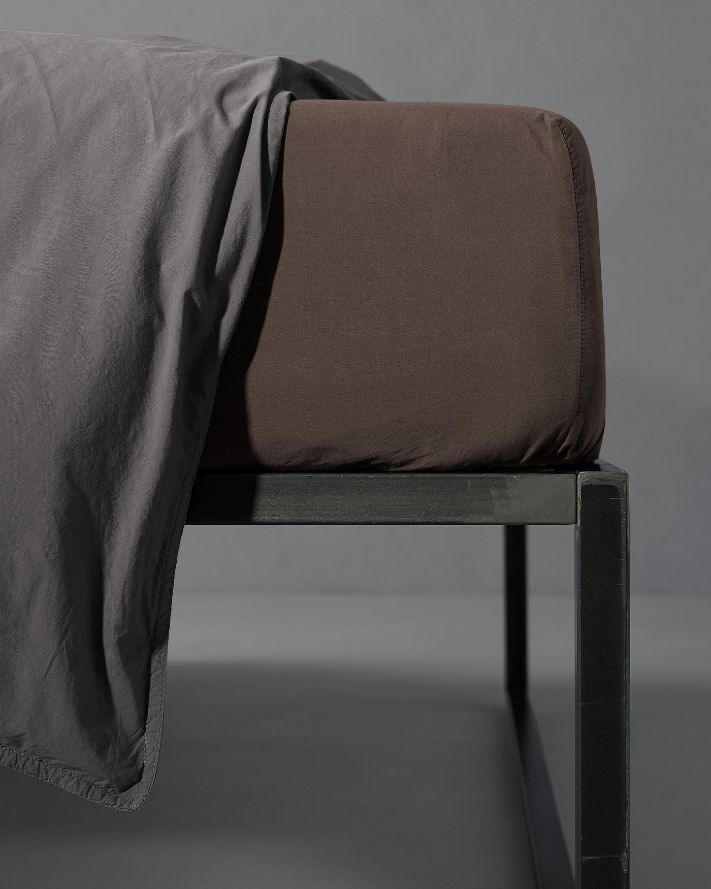 Close-up of espresso fitted sheet on mattress corner with slate flat sheet draped alongside.