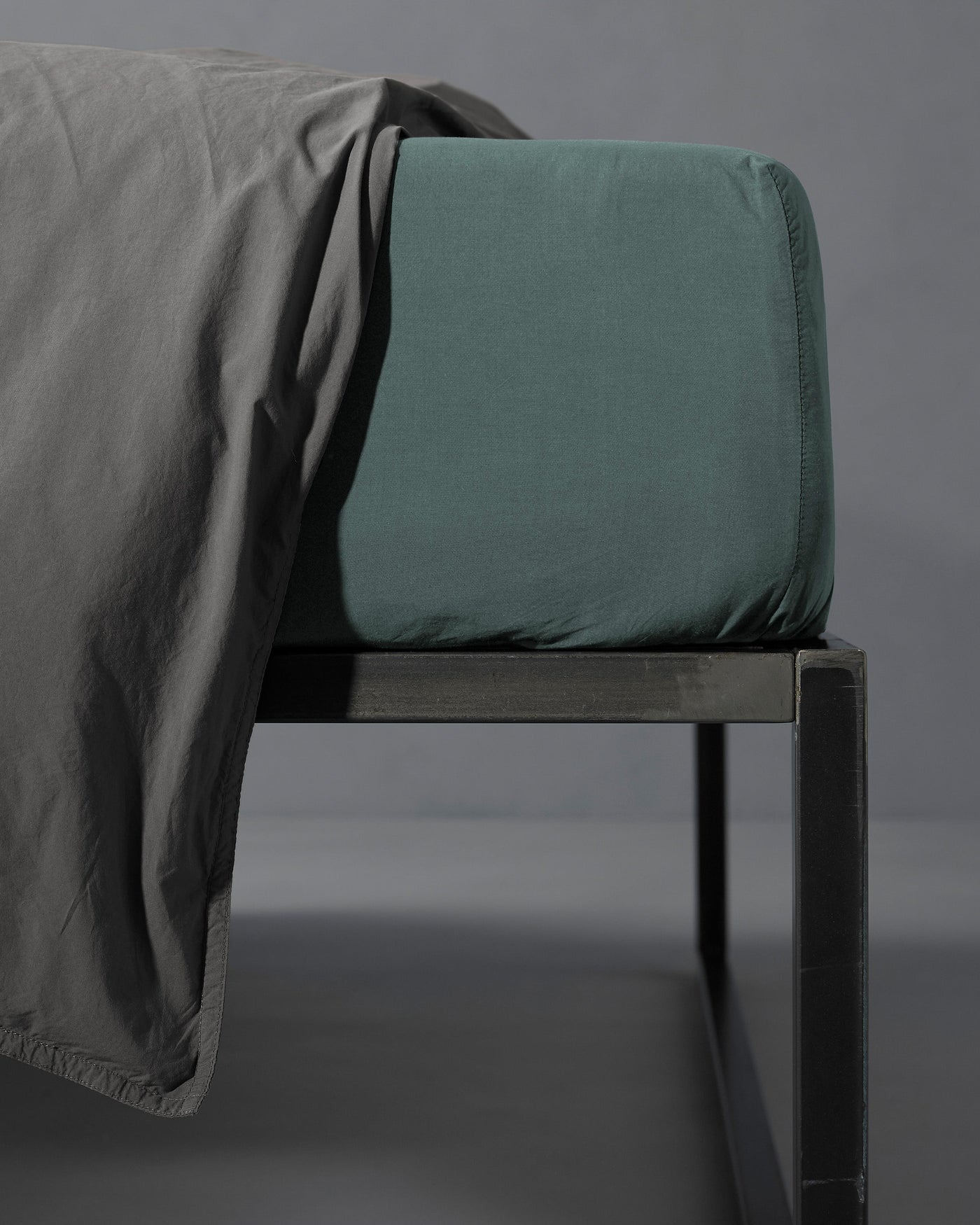 Corner detail of Society Limonta Nite fitted sheet in sage green on a dark metal bed frame.
