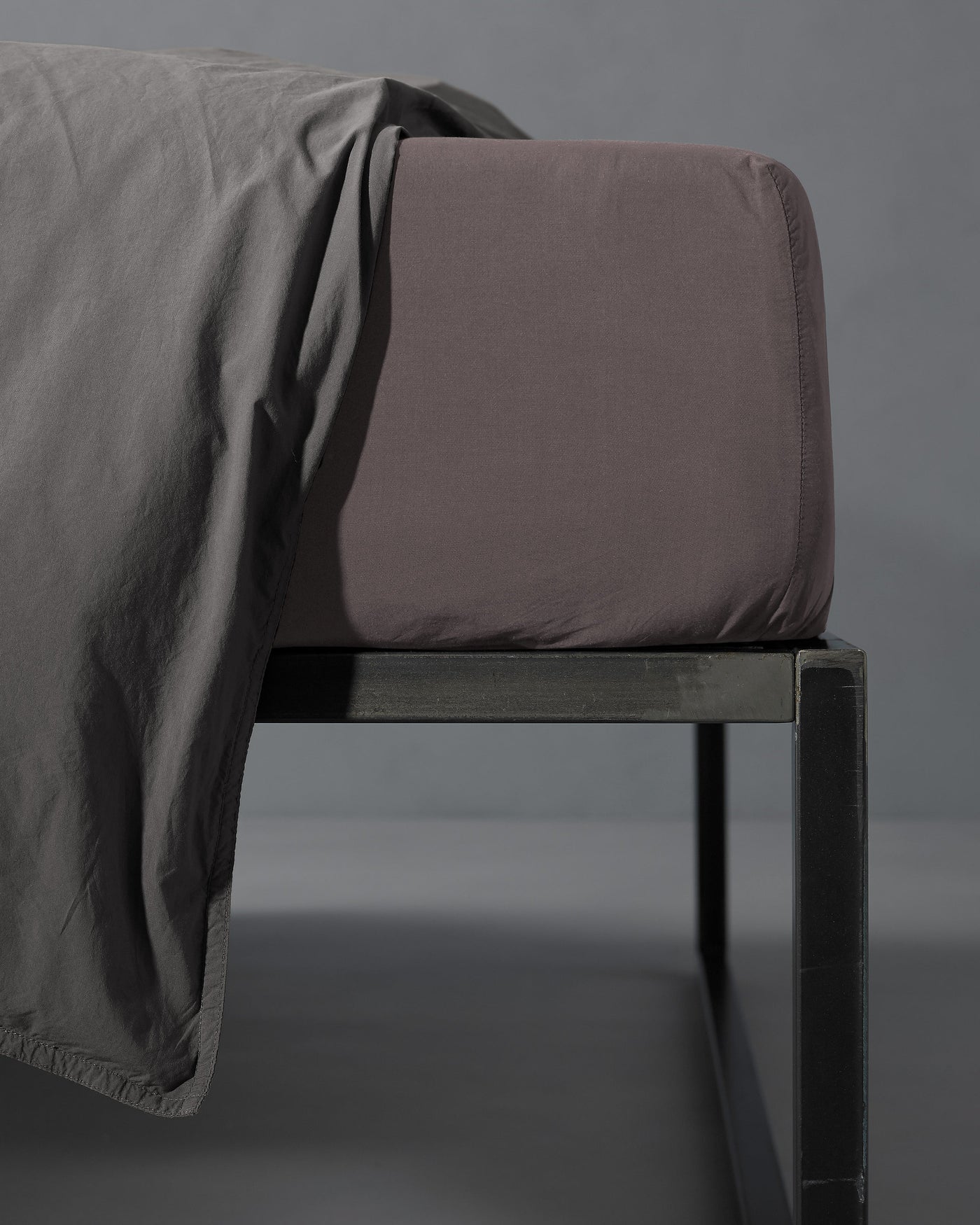 Close-up of Society Limonta Nite fitted sheet corner in mauve on a dark metal bed frame.