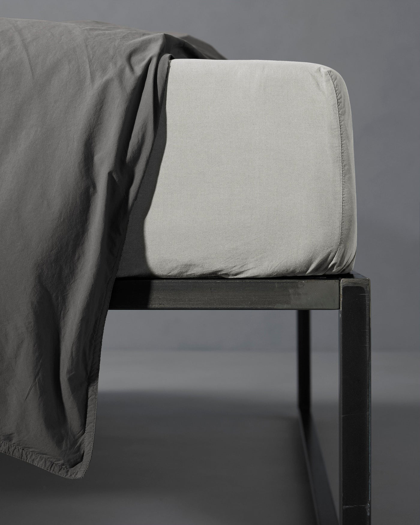 Close-up of Society Limonta Nite fitted sheet corner in stone on a black bed frame.