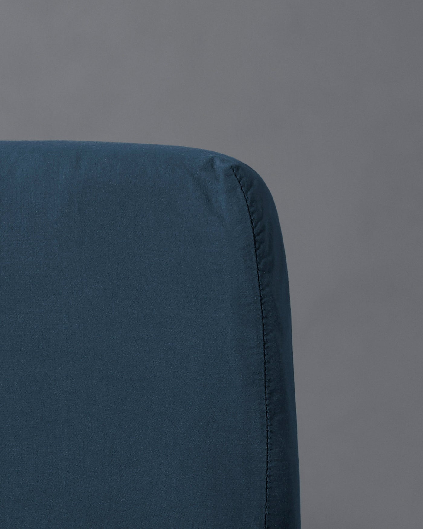 Close-up of midnight blue fitted sheet corner seam on grey background.