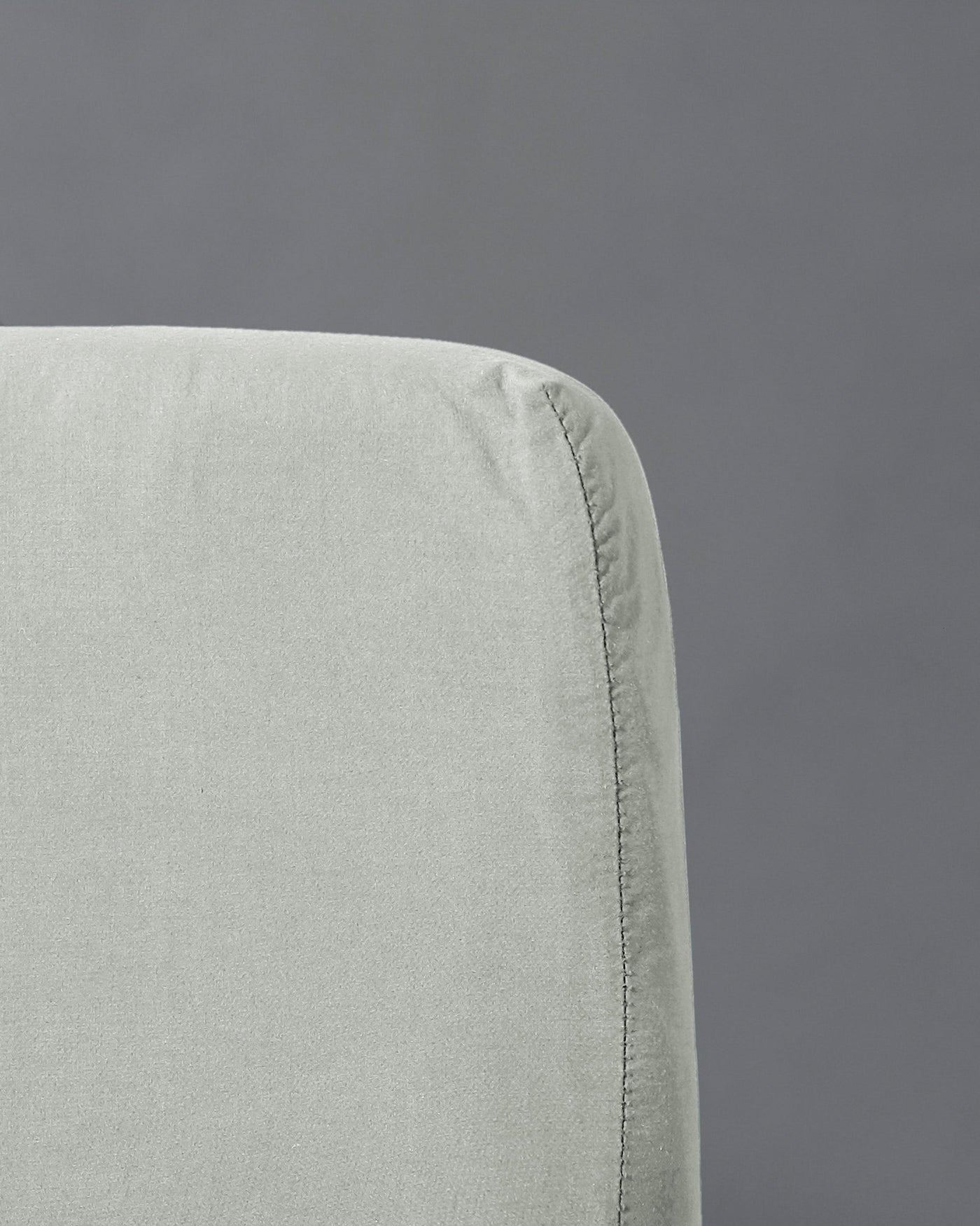 Close-up of fitted sheet corner seam in sage linen against grey background.