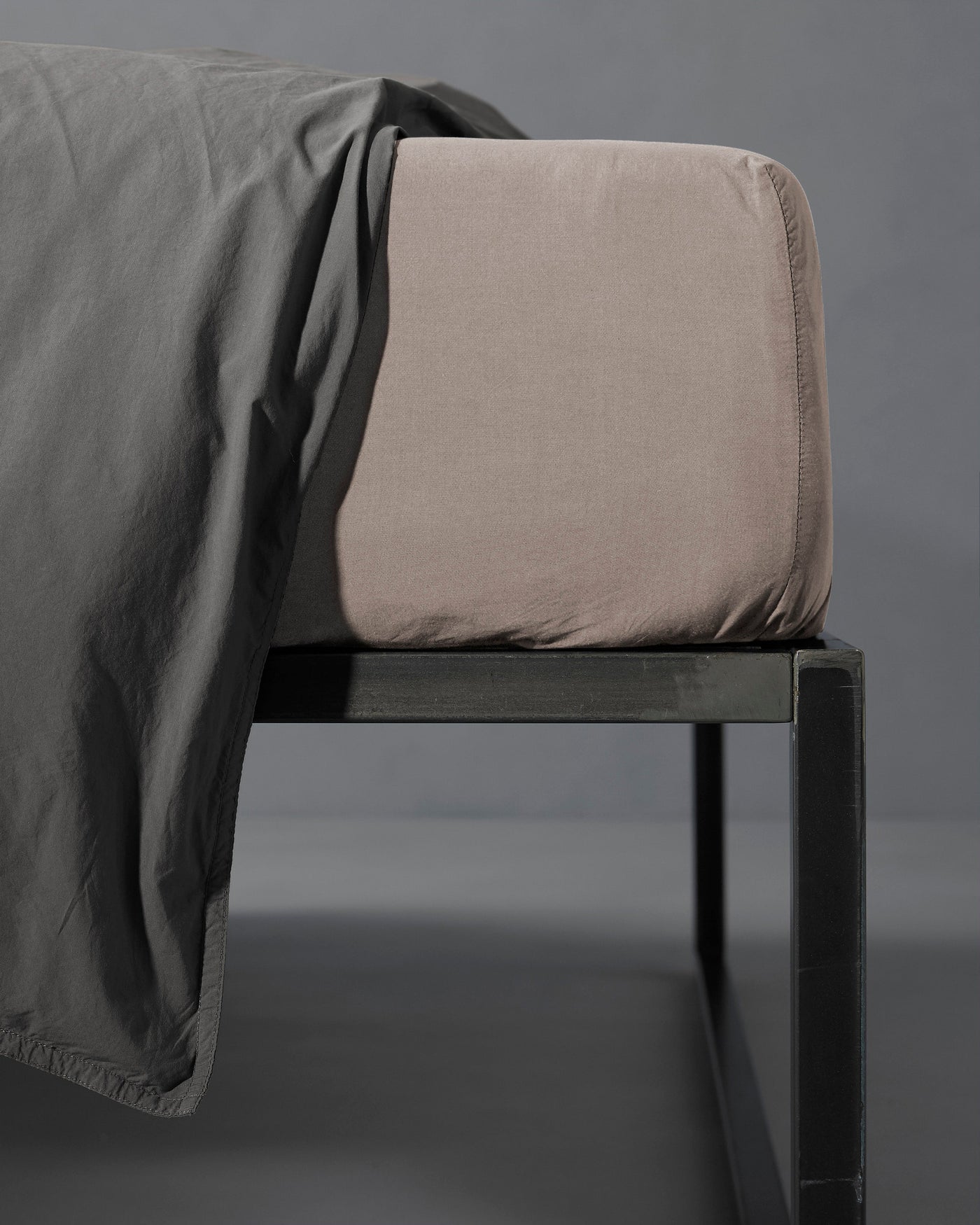 Close-up of a taupe fitted sheet on a mattress corner with charcoal linen draped over.
