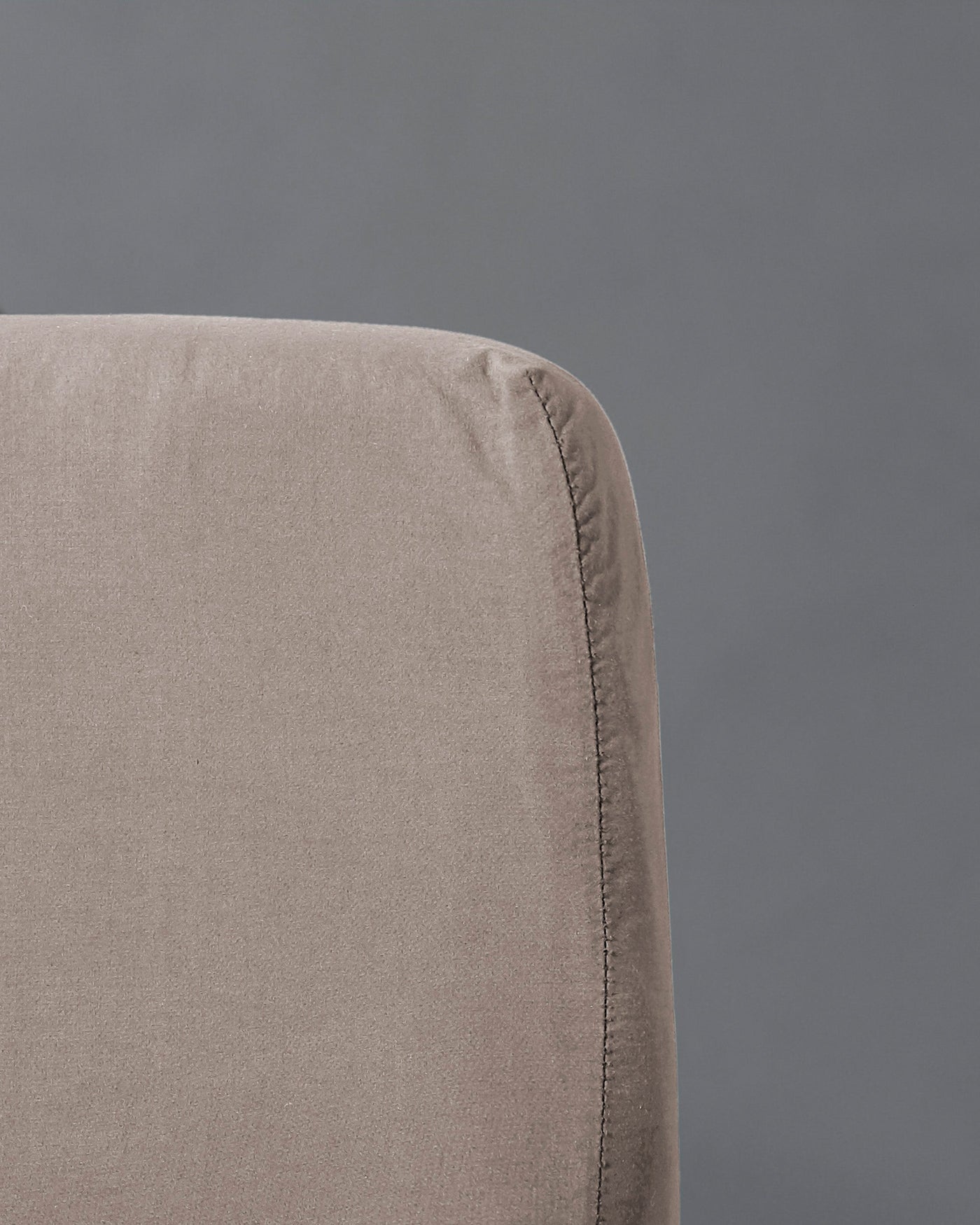 Close-up of taupe linen fitted sheet corner seam against a grey background.