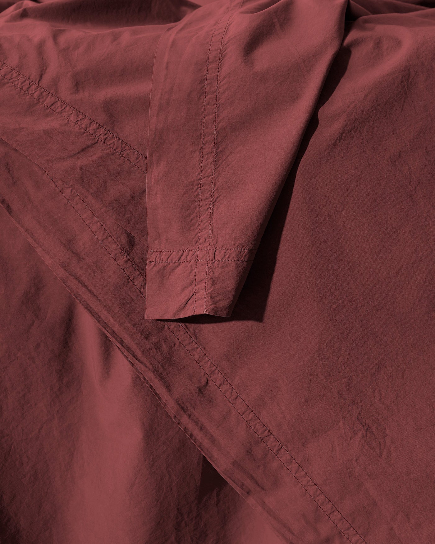 Close-up of Society Limonta Nite flat sheet hem detail in deep burgundy cotton.