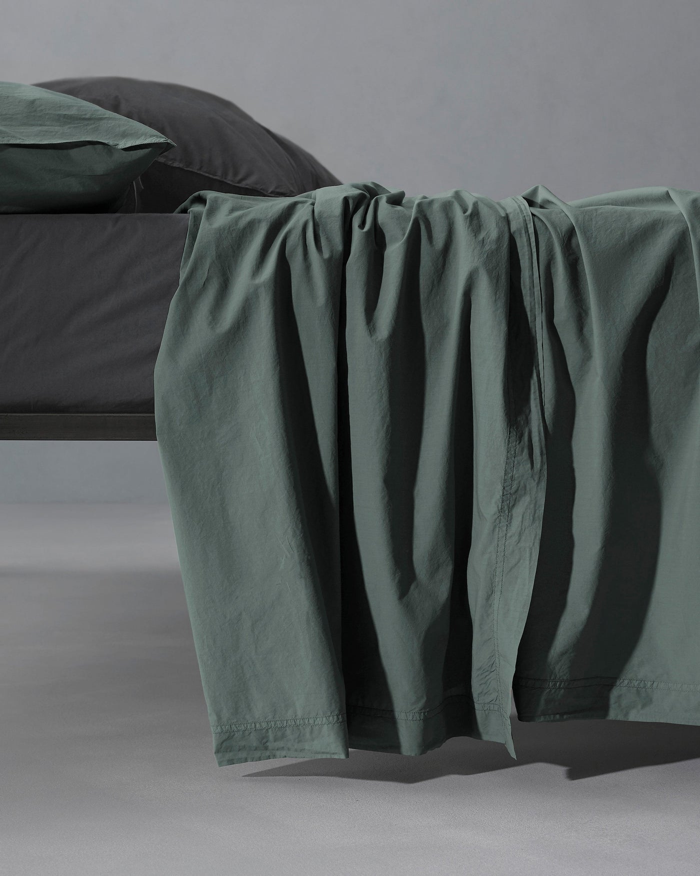 Society Limonta Nite flat sheet in sage draped over bed edge, showing relaxed linen texture.