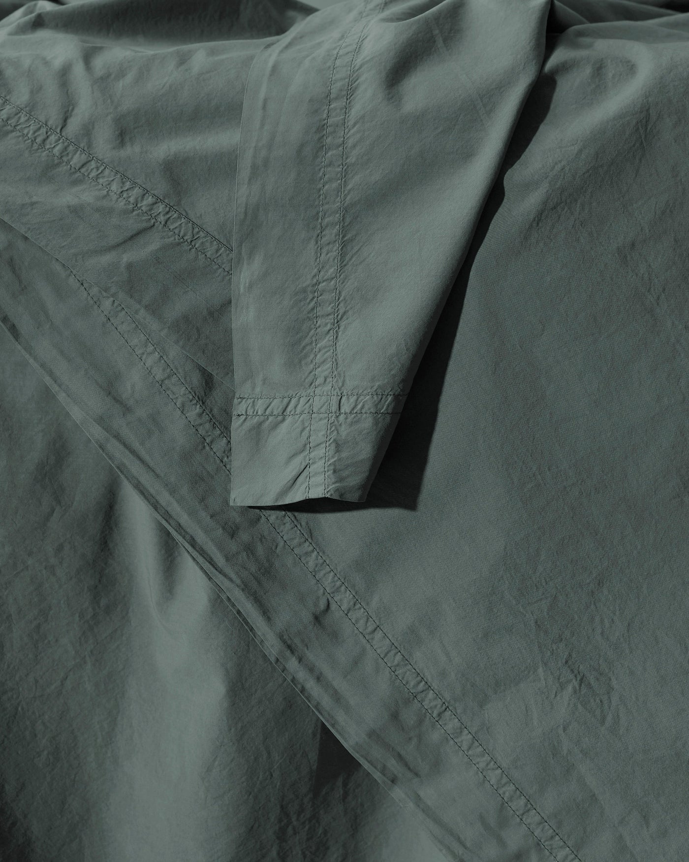 Close-up of Society Limonta Nite duvet cover hem stitching in sage cotton.