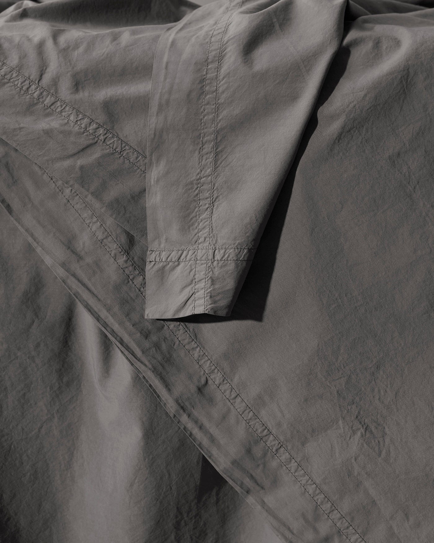 Close-up of slate cotton duvet cover corner with tonal topstitched border detail.