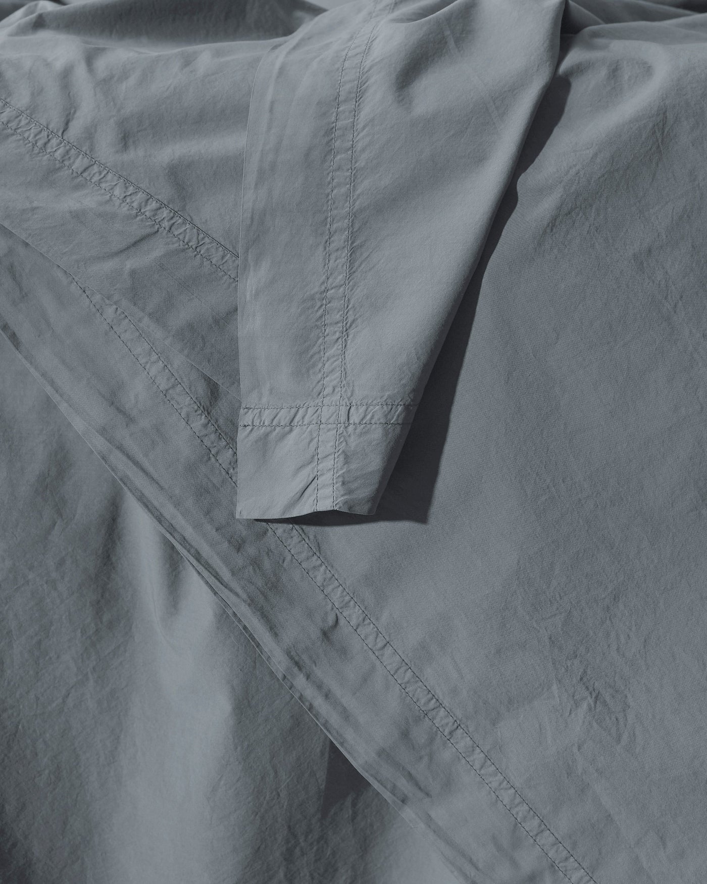 Close-up of slate cotton duvet cover corner with tonal ladder-stitch hem detail.