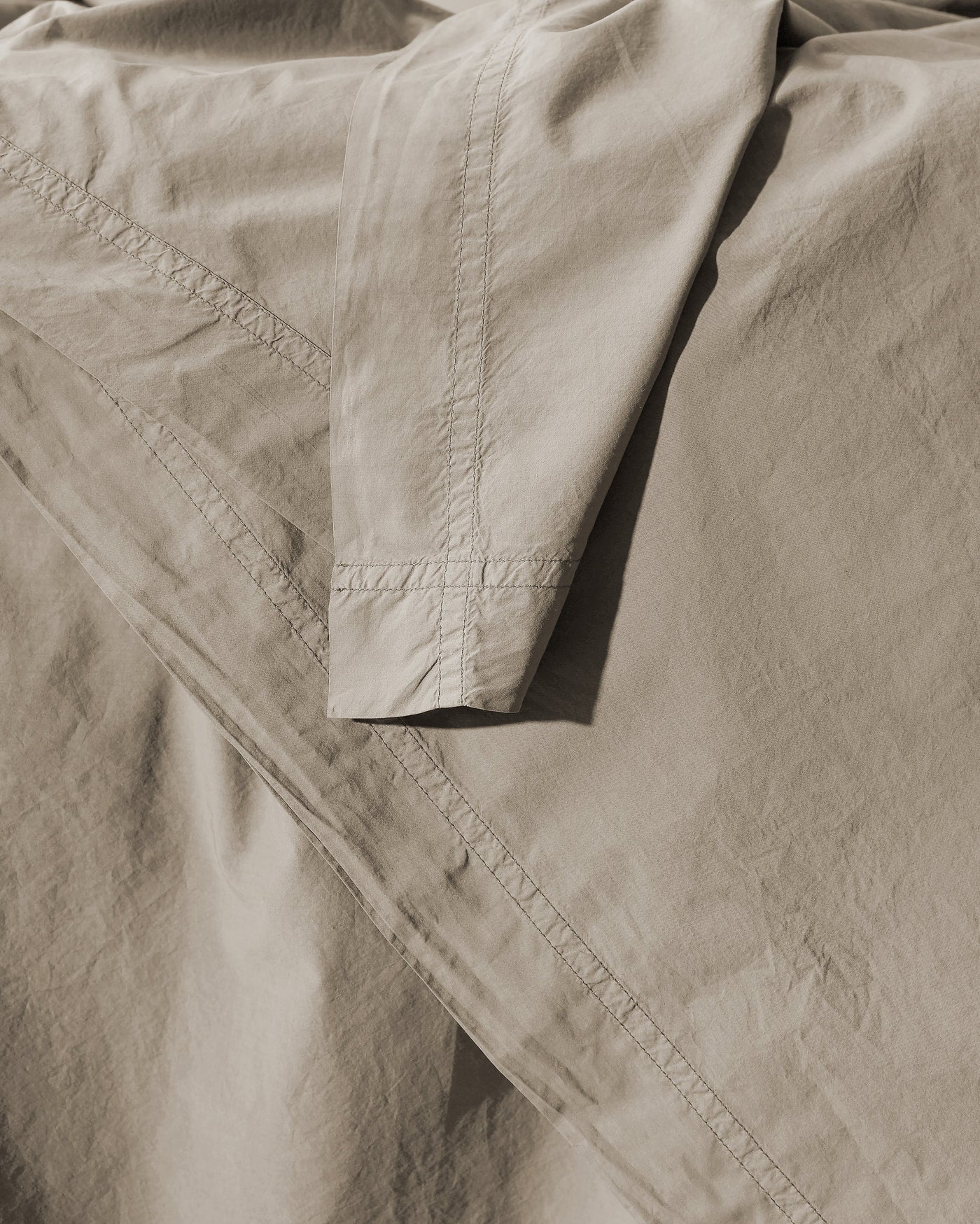 Close-up of Society Limonta Nite duvet cover hem stitching in warm taupe cotton.