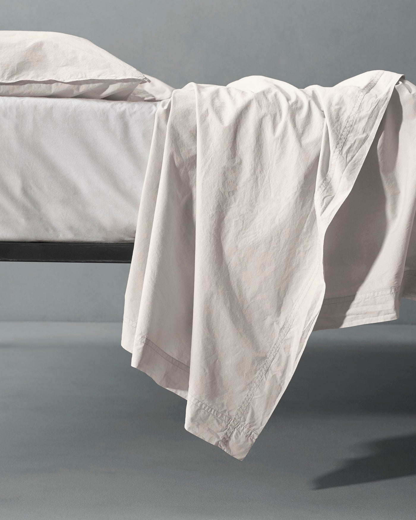 Ivory flat sheet draped over the edge of a black bed frame, floor-length cascade.
