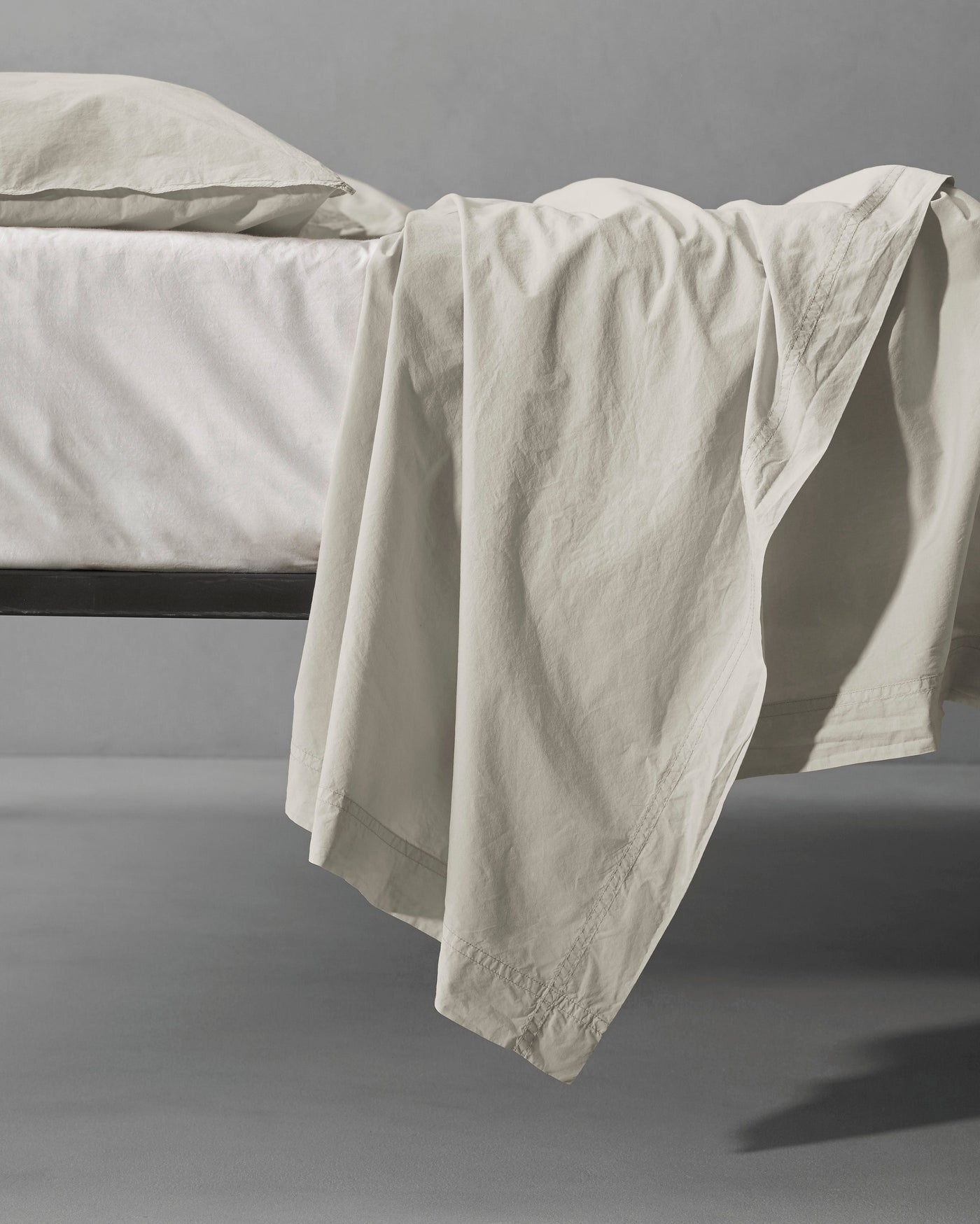 Society Limonta Nite flat sheet in ivory draped over bed edge, relaxed linen texture visible.