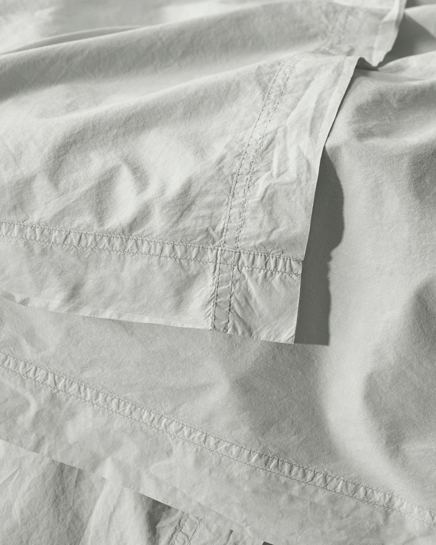 Close-up of ivory cotton duvet cover showing embroidered hem detail and draped folds.