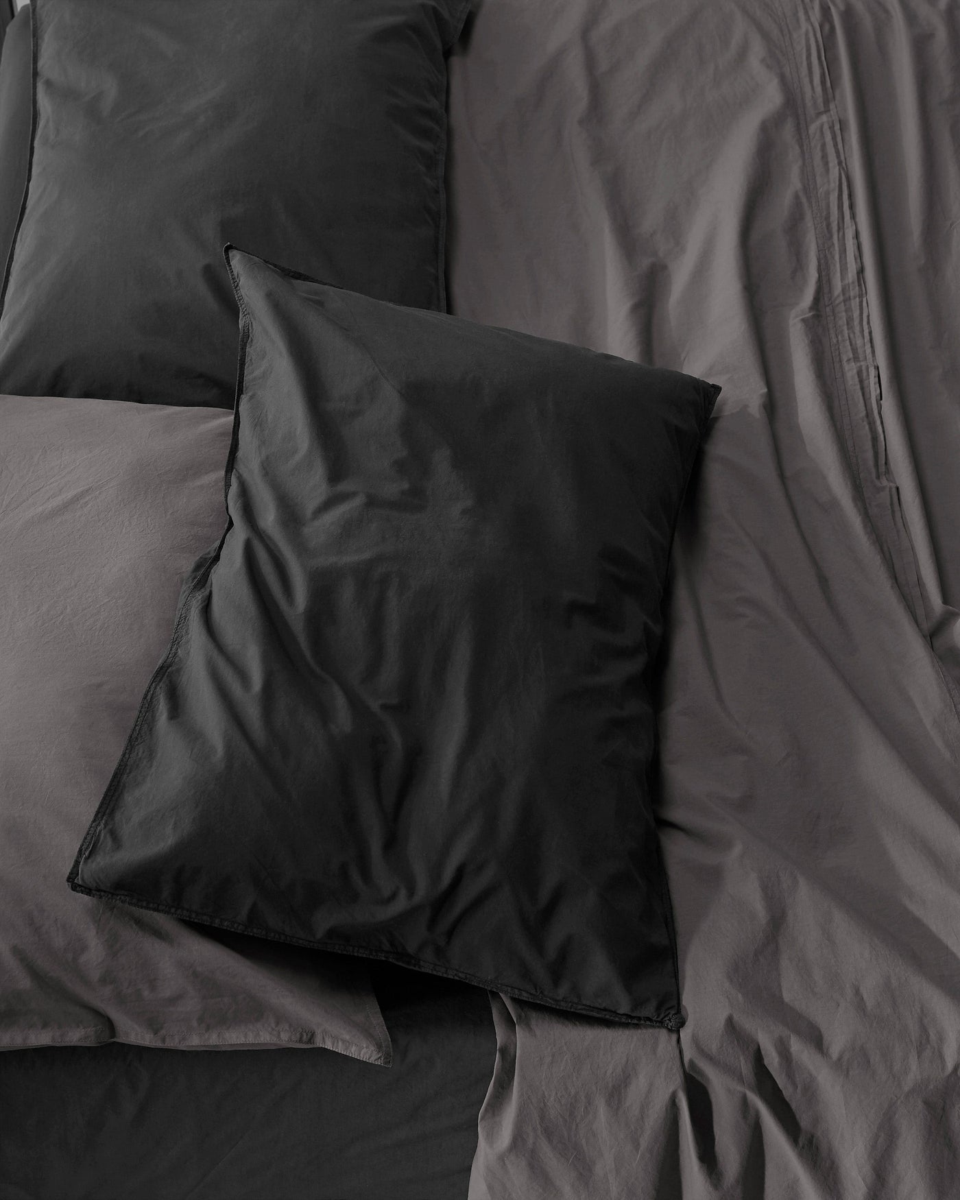 Onyx and charcoal cotton pillowcases layered on a rumpled dark bed, overhead view.