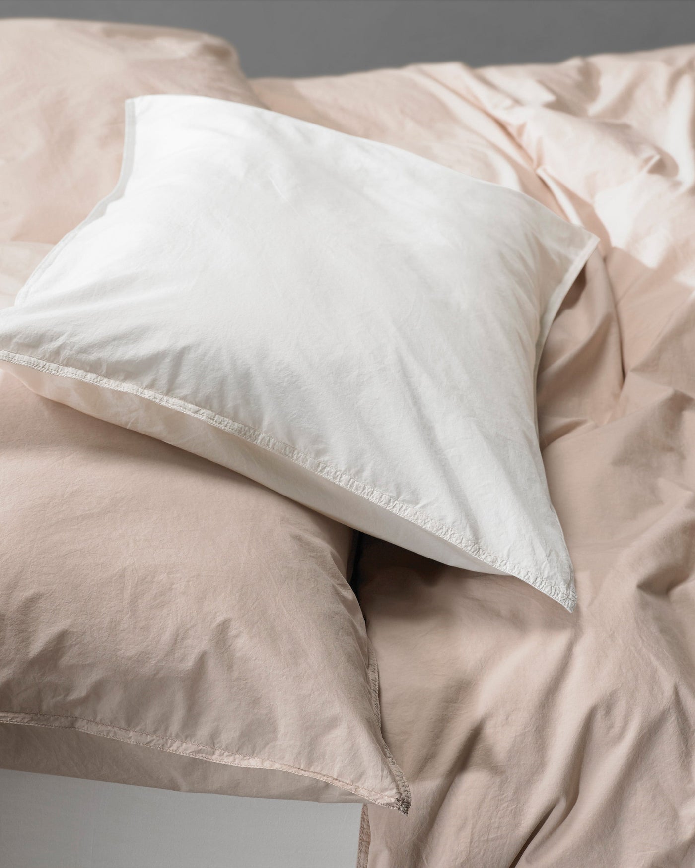 Close-up of ivory and blush cotton pillowcases with soft natural creasing on a made bed.