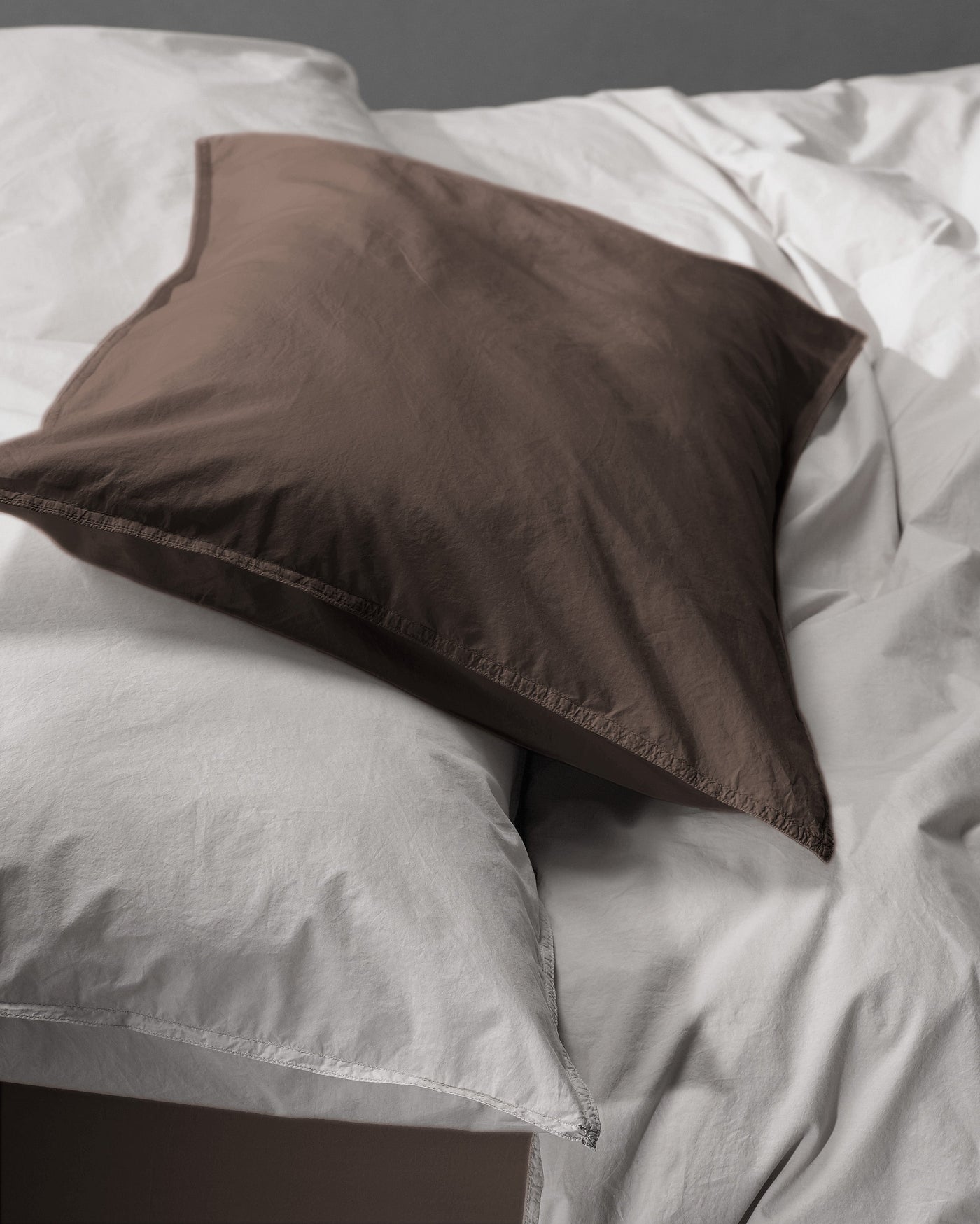 Close-up of a Society Limonta Nite pillowcase in mocha cotton against white bedding.