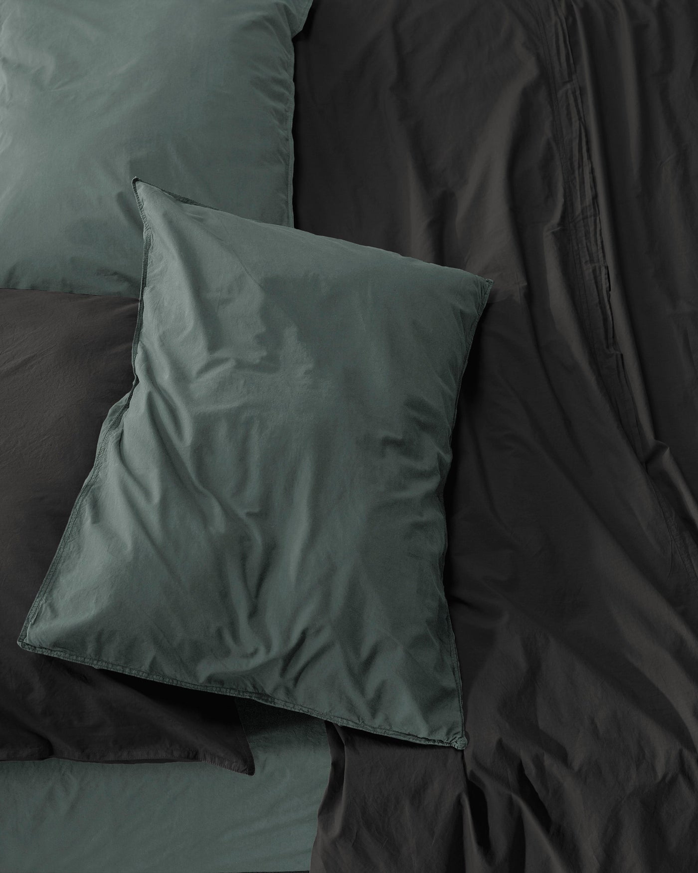Close-up of Society Limonta Nite pillowcases in forest green against charcoal bedding.