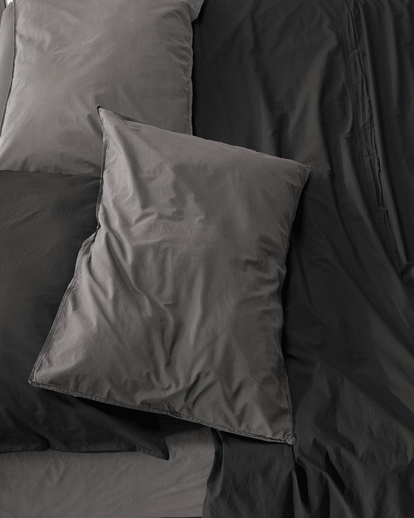 Close-up of Society Limonta Nite pillowcases in charcoal cotton, shown layered on tonal bedding.