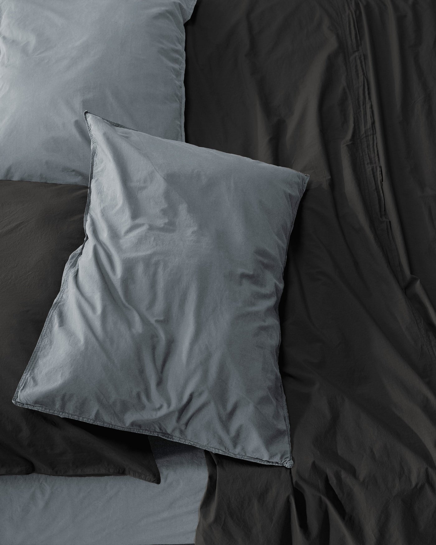 Slate and charcoal cotton pillowcases layered on dark bedding, overhead view.