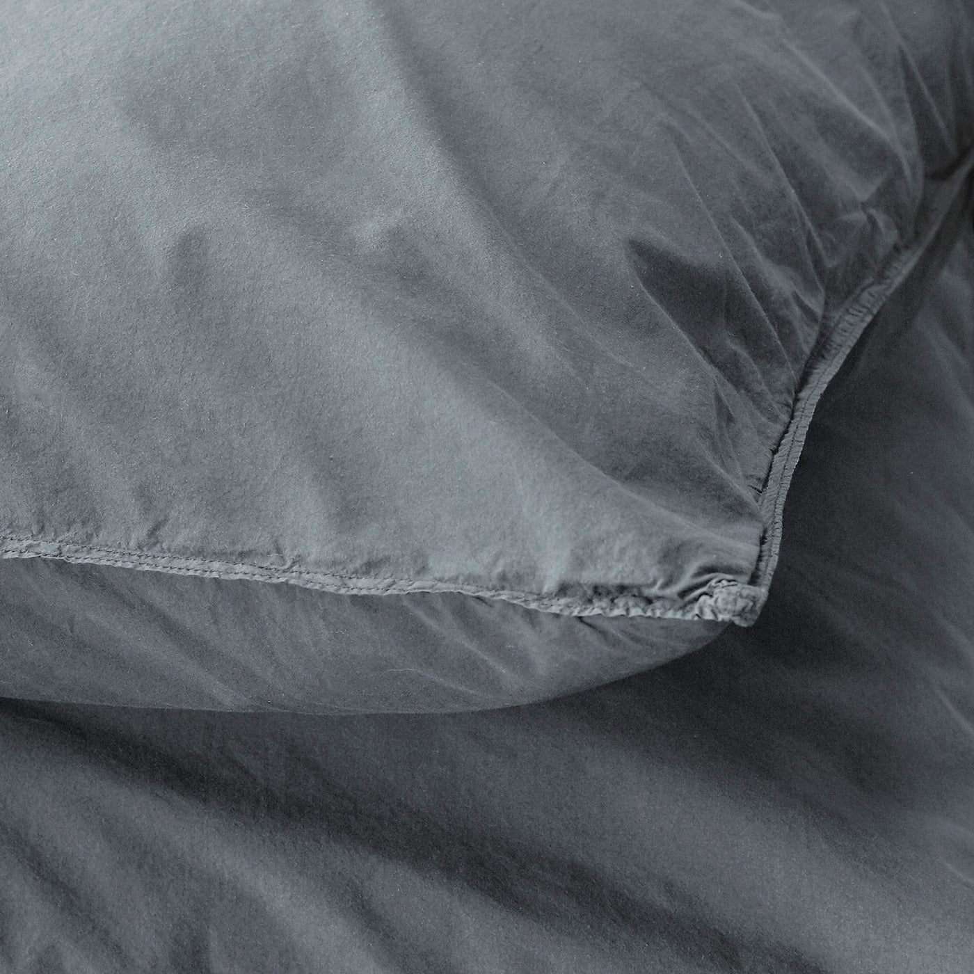 Close-up of slate linen pillowcase corner seam detail showing relaxed texture.