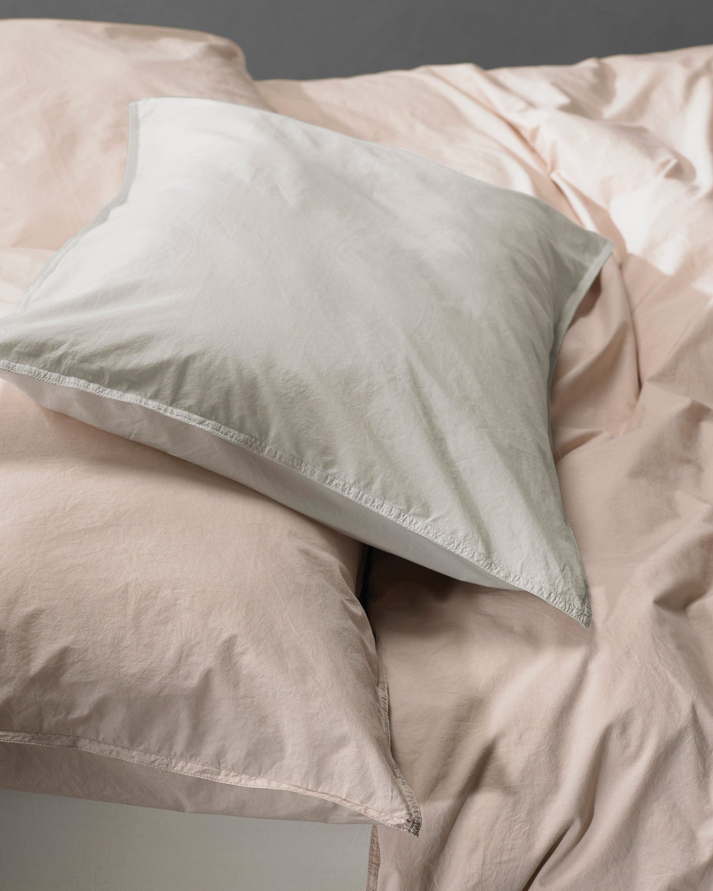 Close-up of sage and blush cotton pillowcases with subtle texture and soft drape.