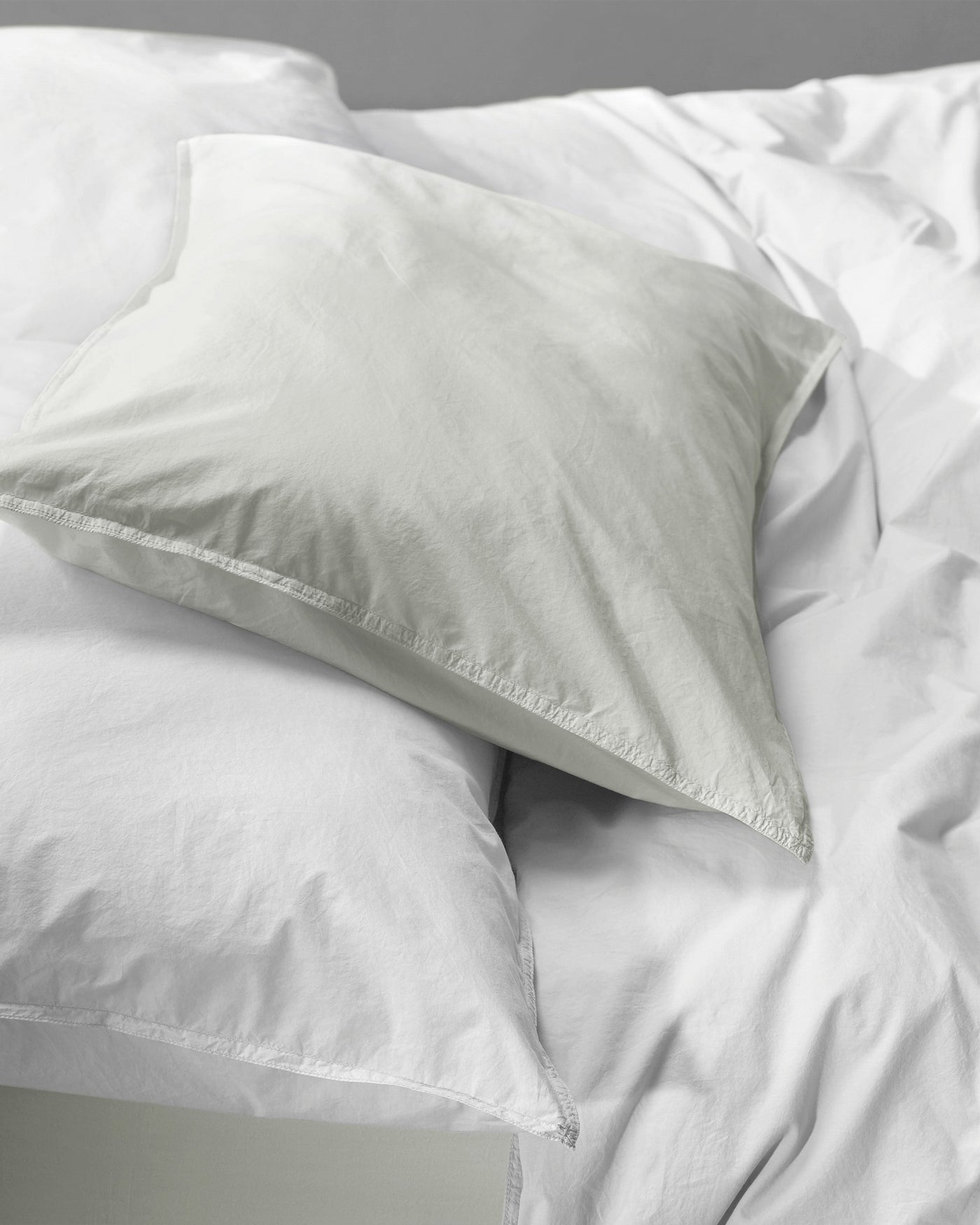 Close-up of a Society Limonta Nite pillowcase in sage atop white bedding, showing relaxed cotton texture.