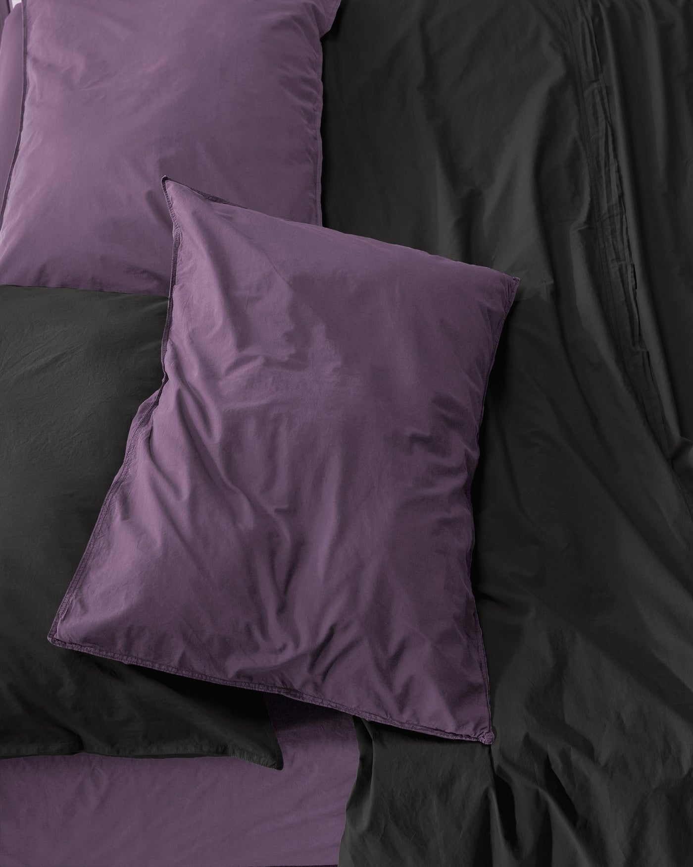 Close-up of plum pillowcases layered against a charcoal duvet, smooth sateen finish.
