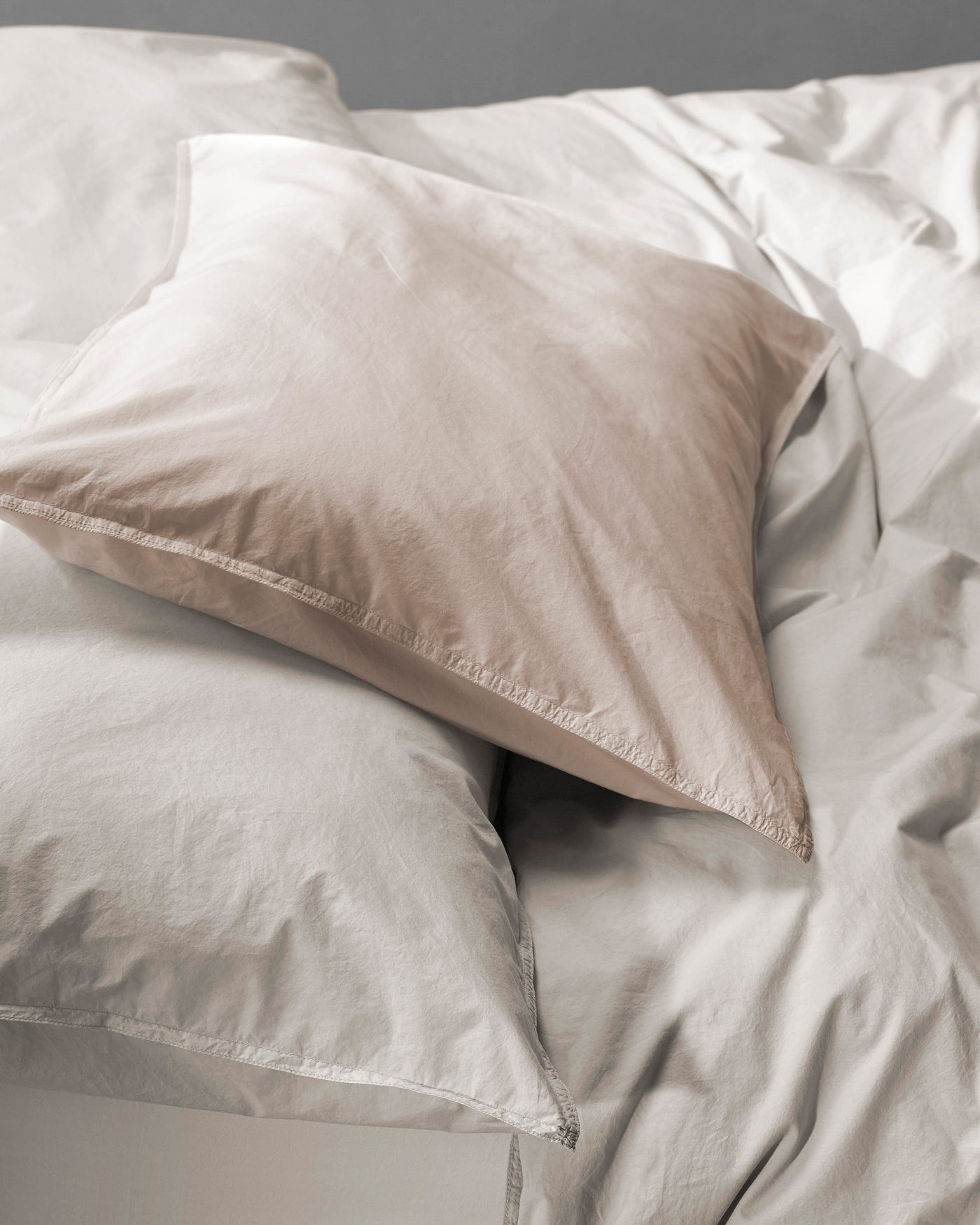 Close-up of a sand pillowcase layered over white cotton bedding, softly rumpled.