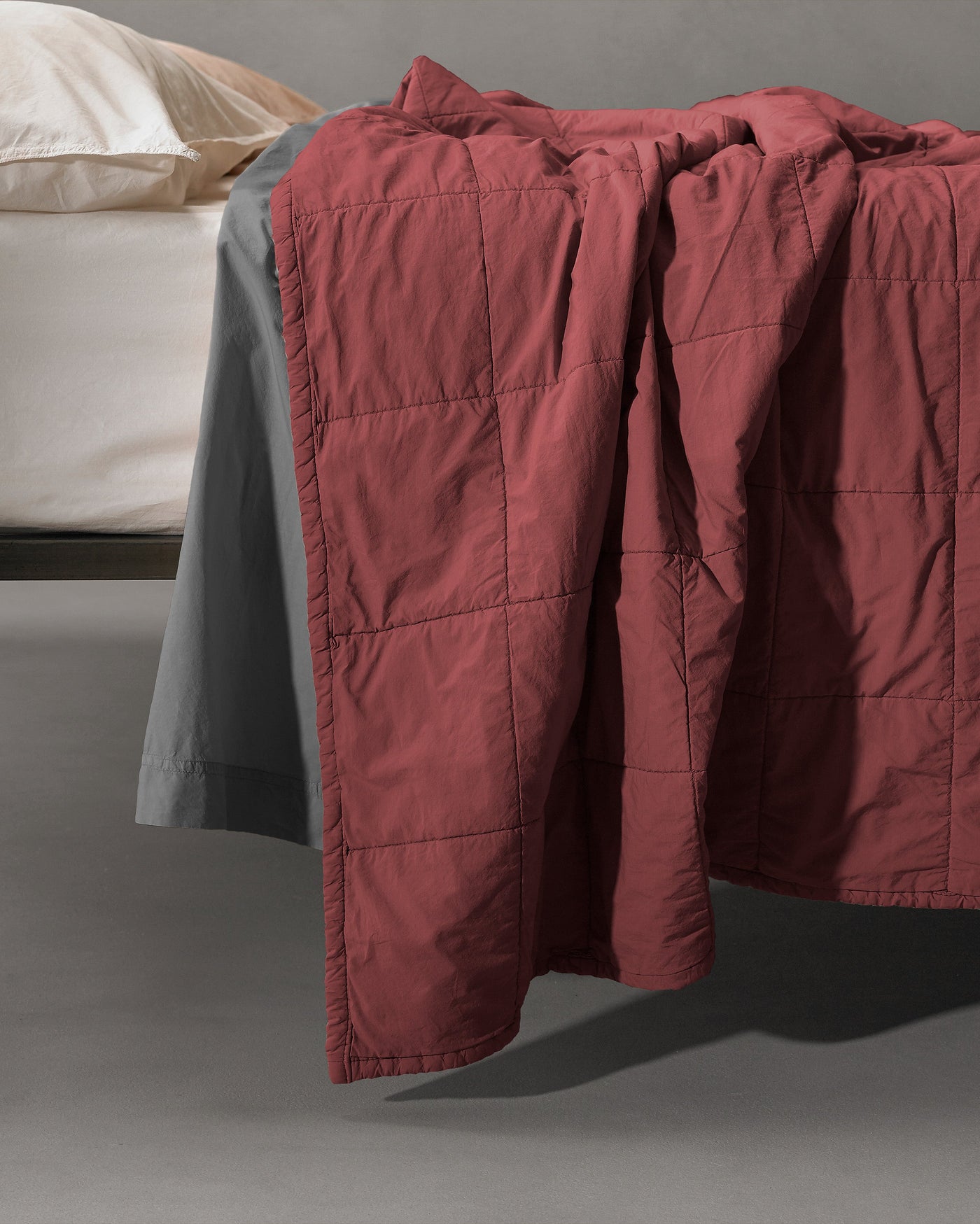 Close-up of Society Limonta Nite quilt in crimson, draped over bed edge showing grid stitching.