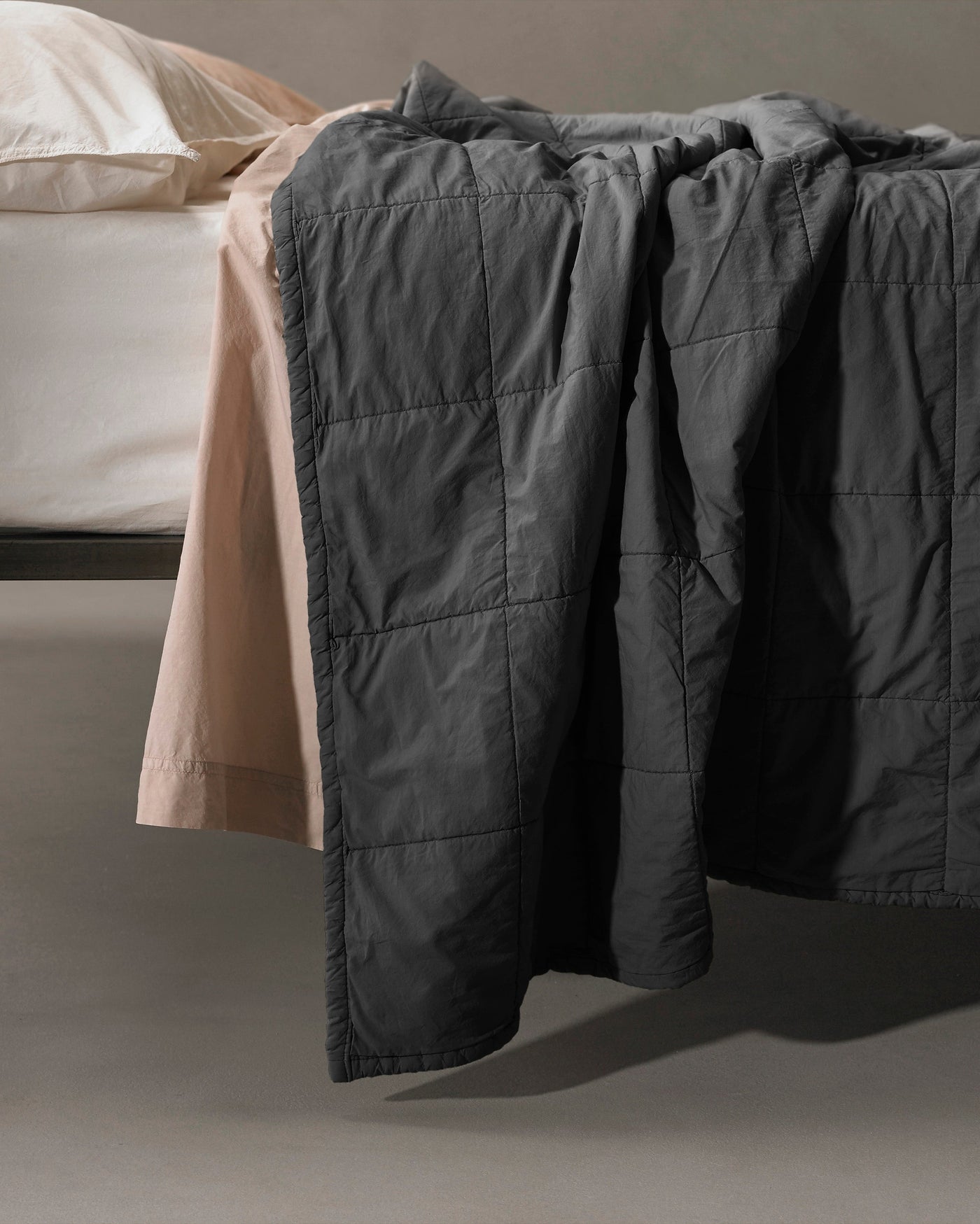 Close-up of Society Limonta Nite quilt in charcoal, draped over bed edge showing grid-stitched texture.