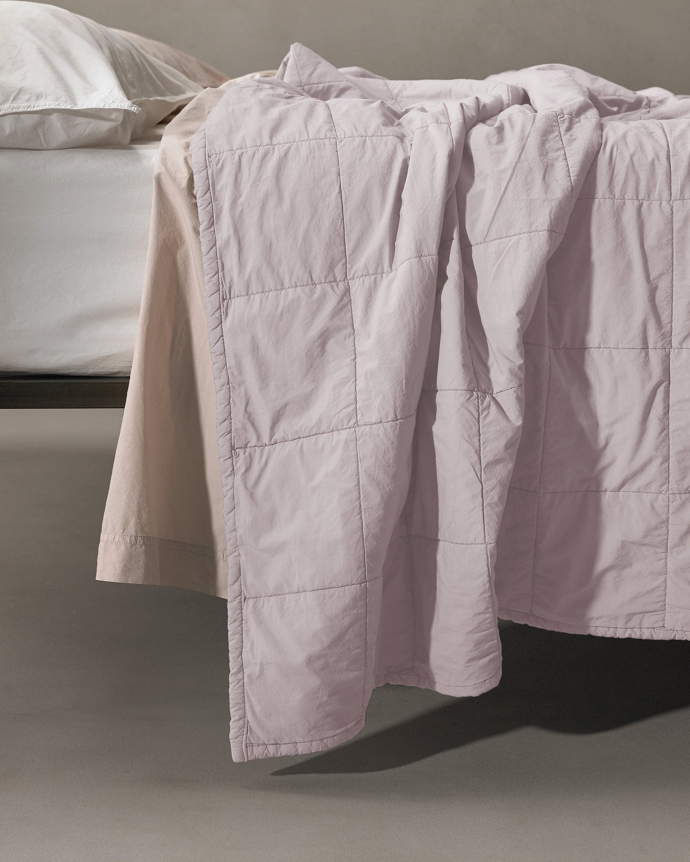 Blush quilted coverlet draped over bed edge, showing large square stitching pattern.
