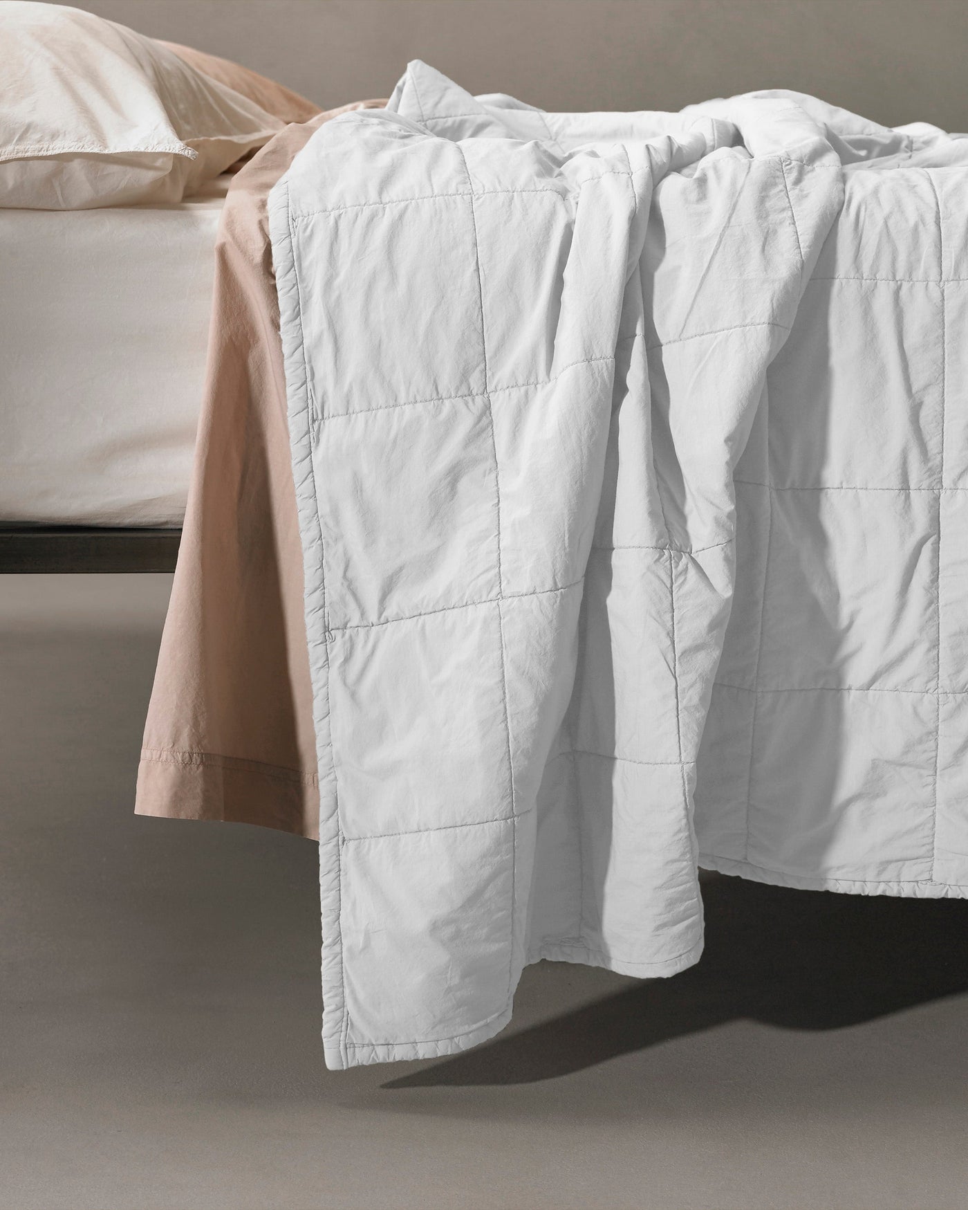 White Society Limonta Nite quilt draped over bed edge, showing grid-stitched panel detail.