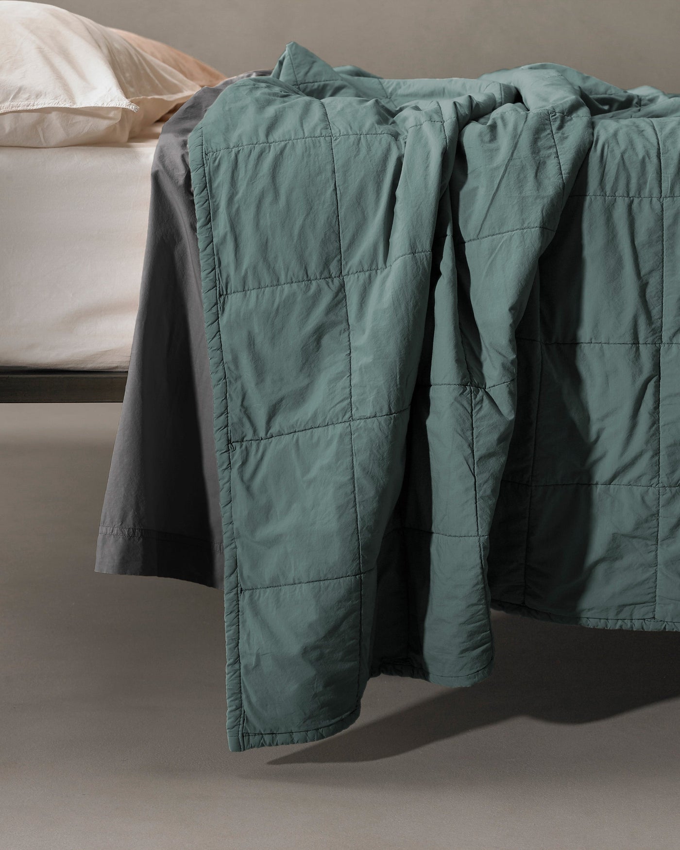 Close-up of Society Limonta Nite quilt in sage green with grid stitching, draped over bed edge.