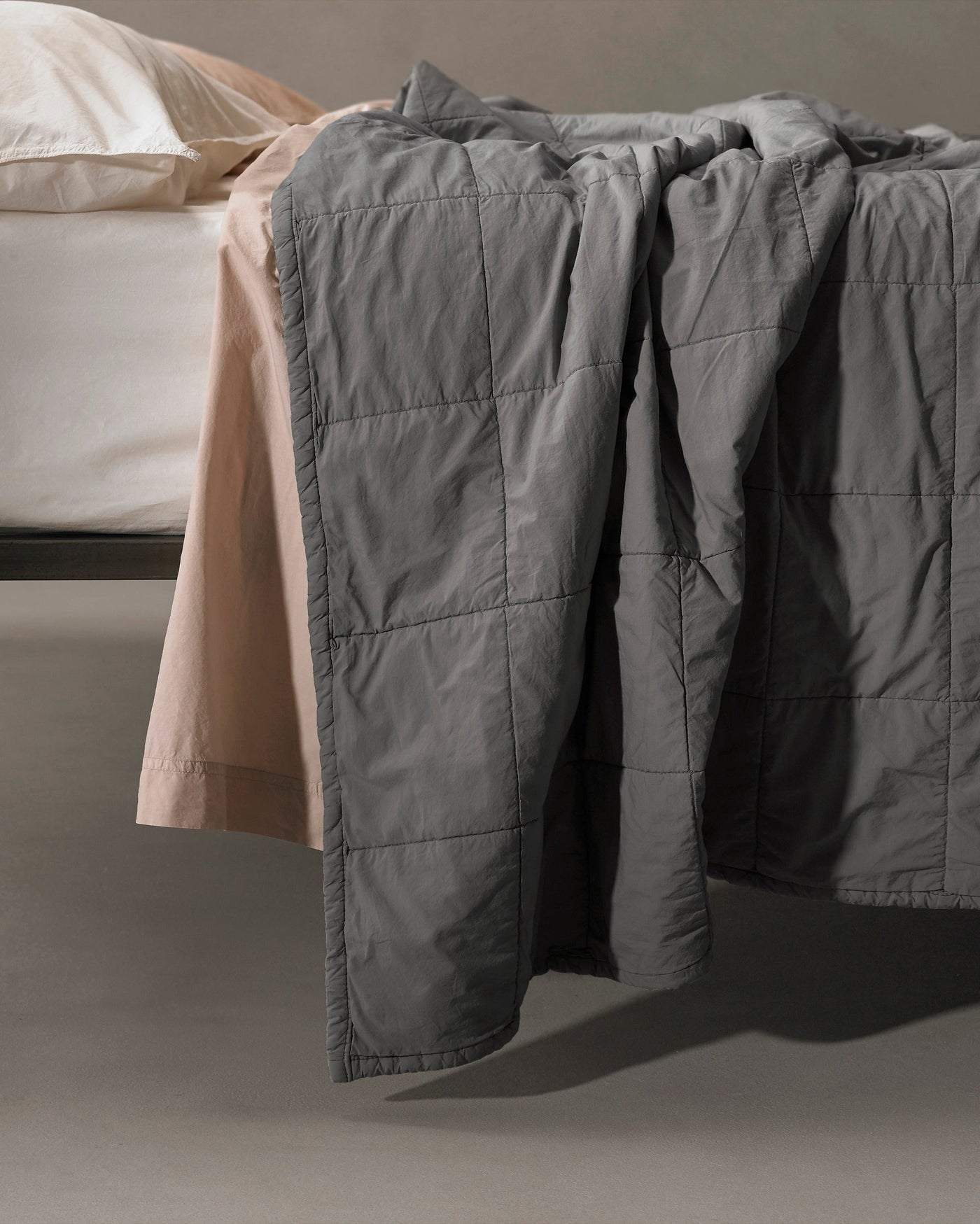 Close-up of Society Limonta Nite quilt in slate grey with grid quilting, draped over bed edge.