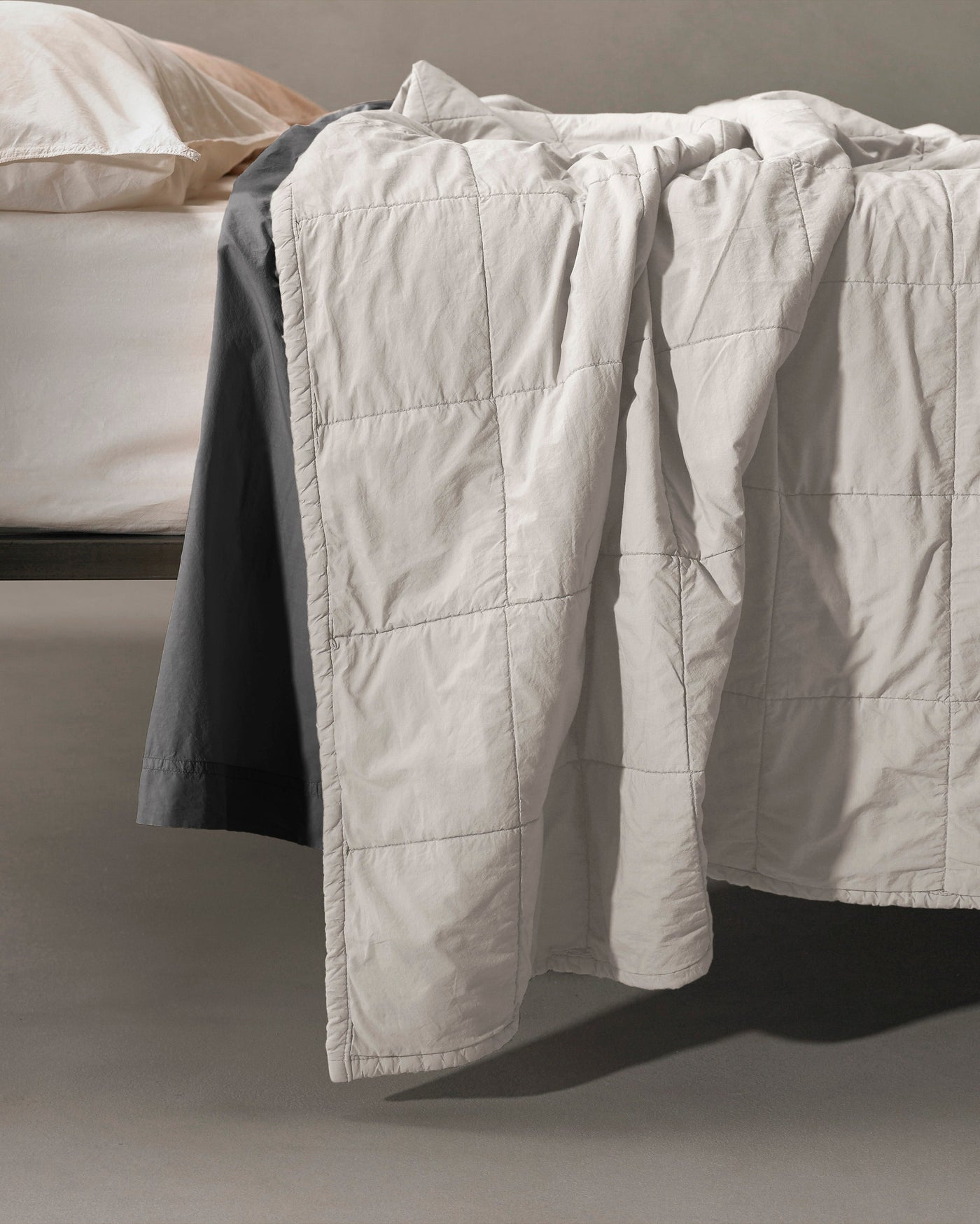 Close-up of Society Limonta Nite quilt in ivory with grid stitching draped over bed edge.