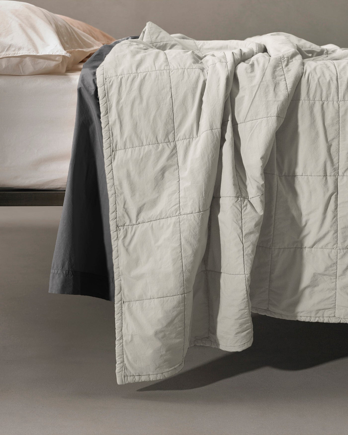 Close-up of Society Limonta Nite quilt in pearl, showing grid-stitched panels draped over bed edge.