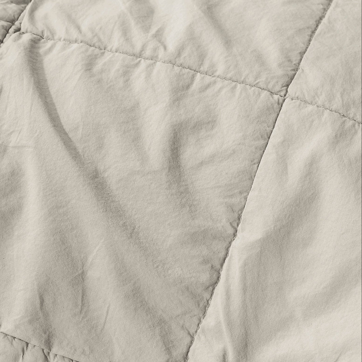 Close-up of ivory linen quilt showing diamond quilting stitches and softly rumpled texture.