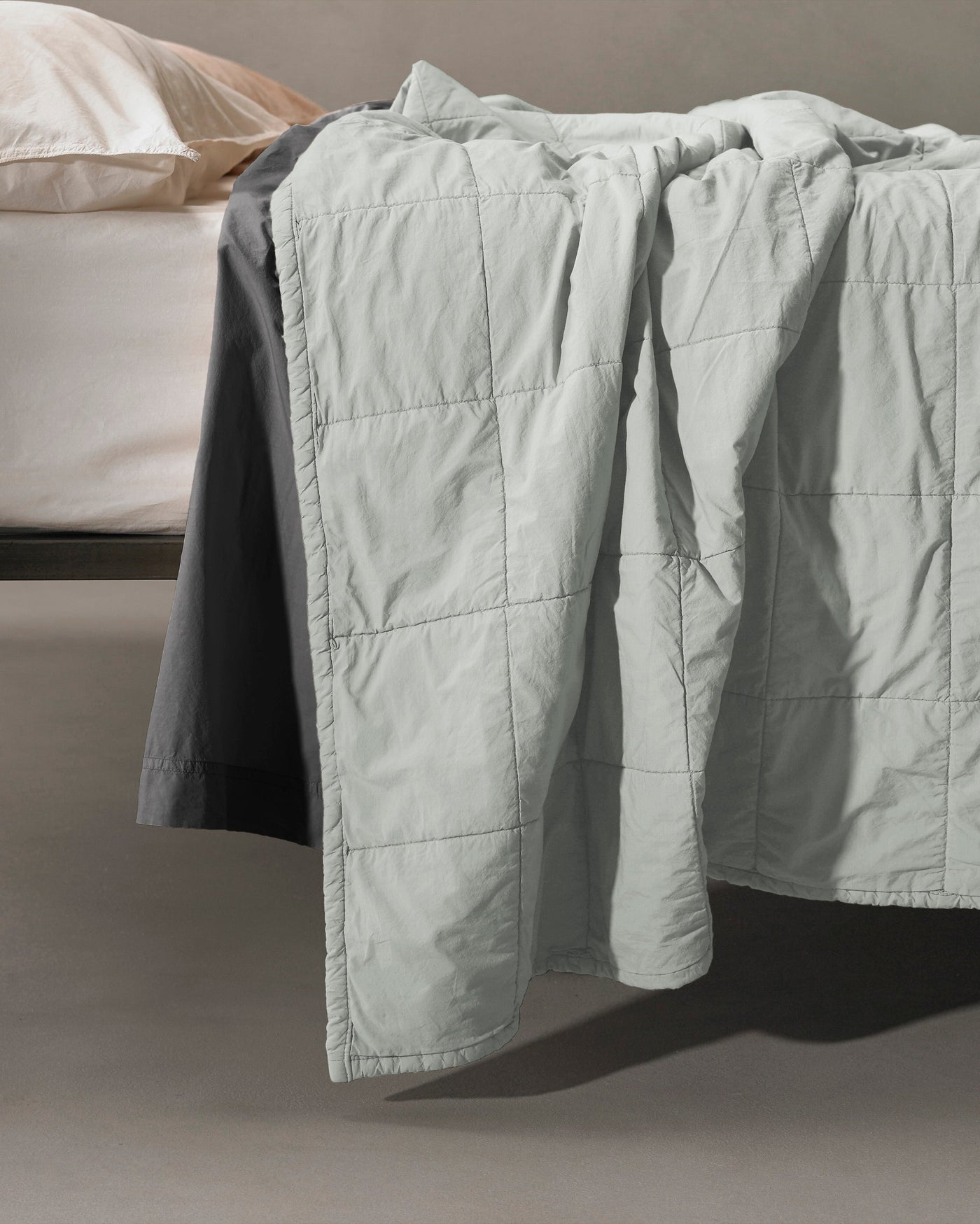 Close-up of Society Limonta Nite quilt's grid-stitch quilting in mist draping over bed edge.