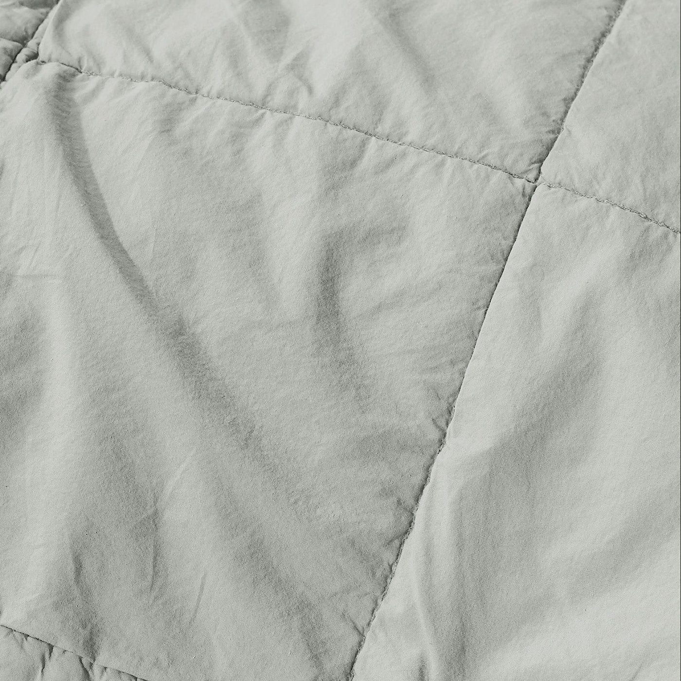 Close-up of sage linen quilt showing diamond quilting stitchwork and textured fabric surface.