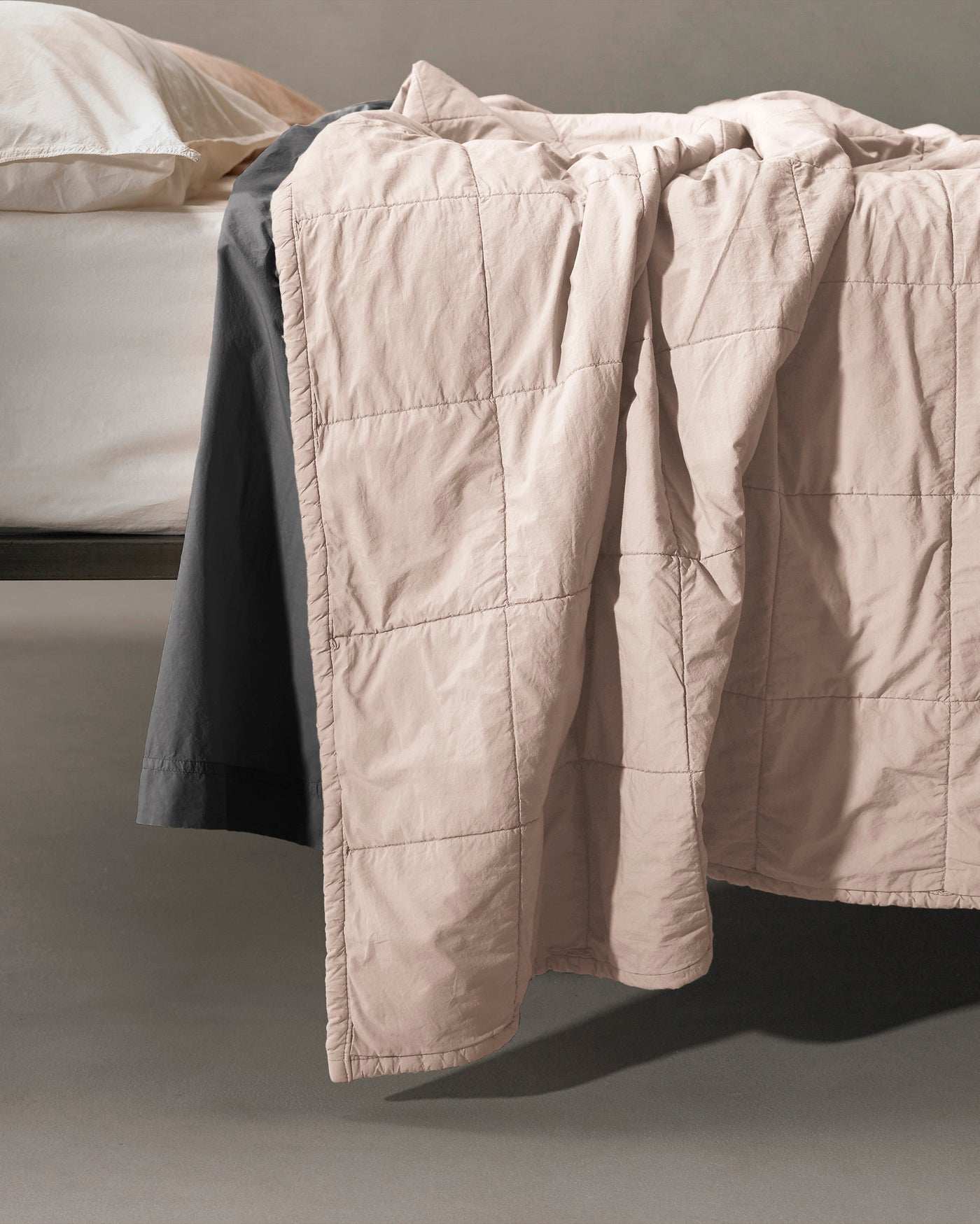Close-up of Society Limonta Nite quilt in blush, draped over bed edge showing grid quilting detail.