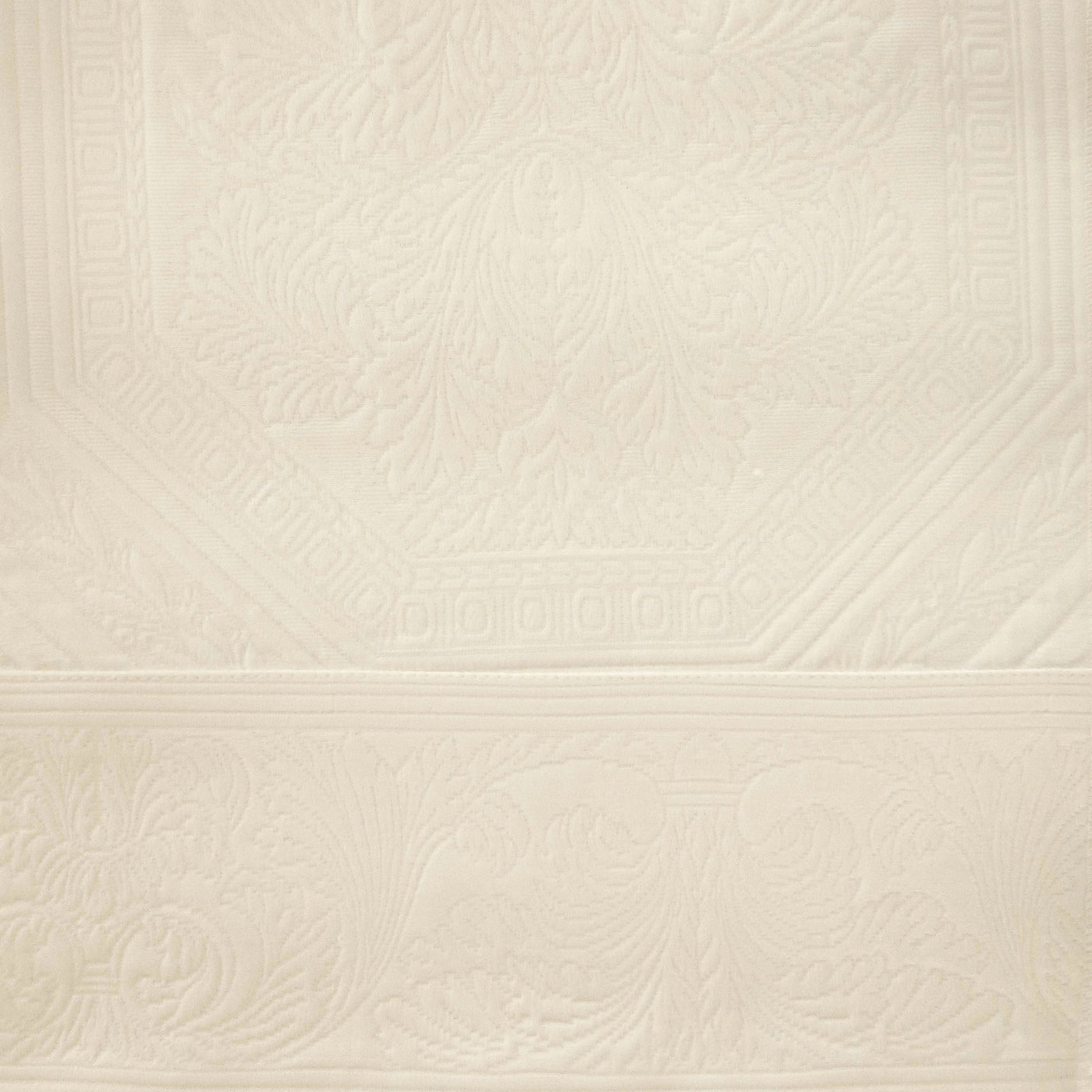 Close-up of ivory matelassé coverlet with ornate floral and scrollwork embossed pattern.