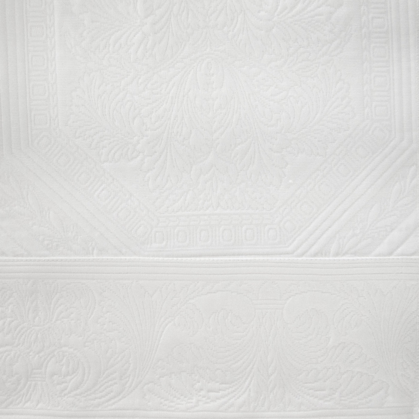 Close-up of white Olympia pillow sham showing ornate jacquard floral and scroll border detail.