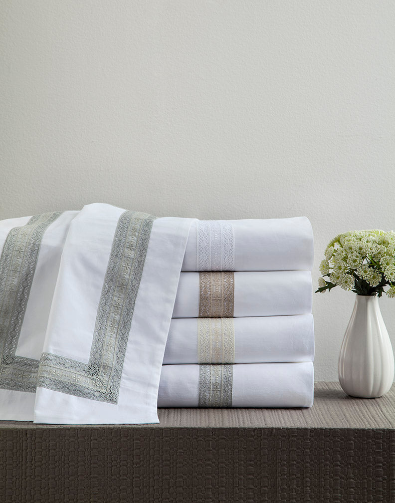Close-up of folded white Pamela sheets with embroidered border in sage, taupe, and ivory colorways.