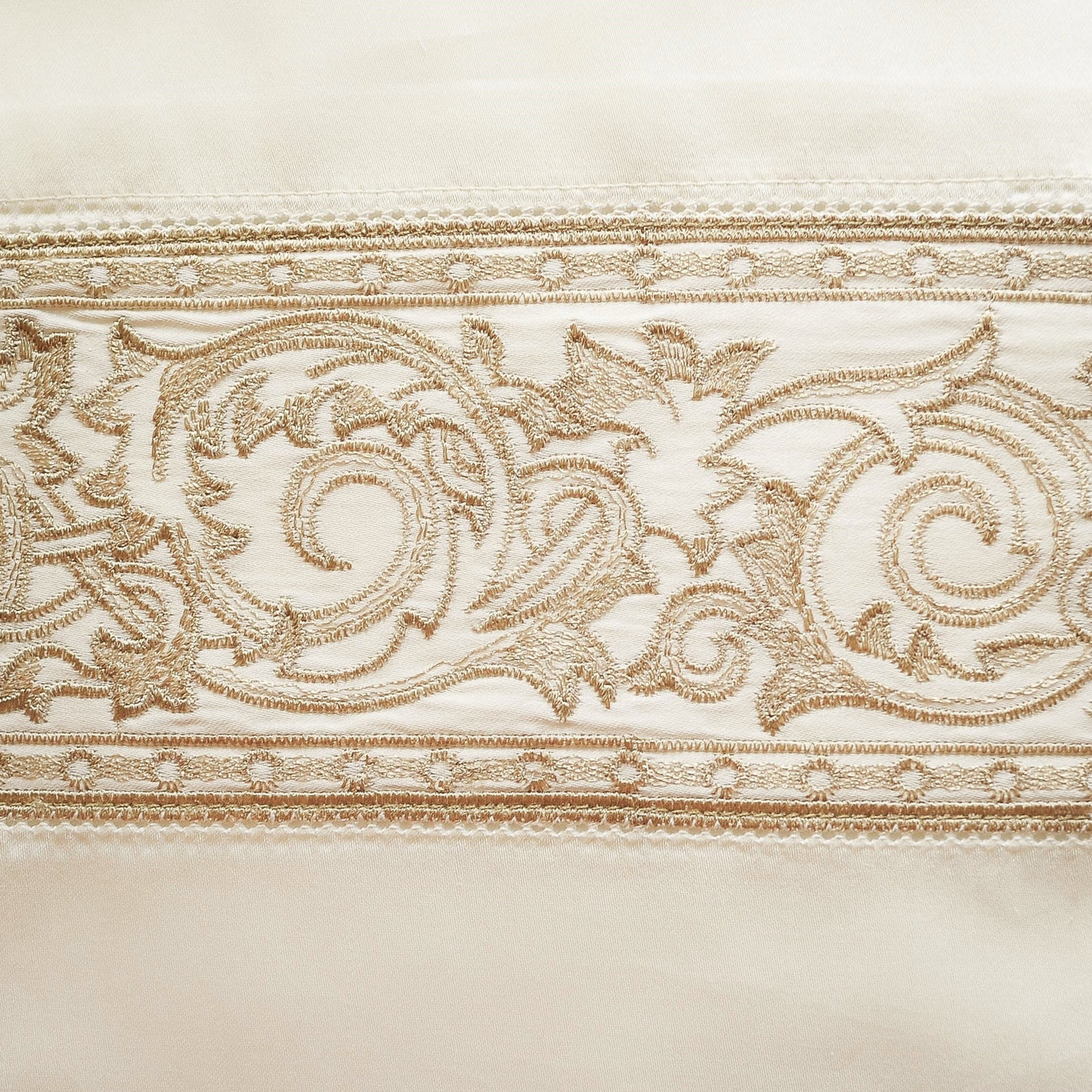 Close-up of champagne embroidered acanthus scroll border on ivory linen pillowcase.